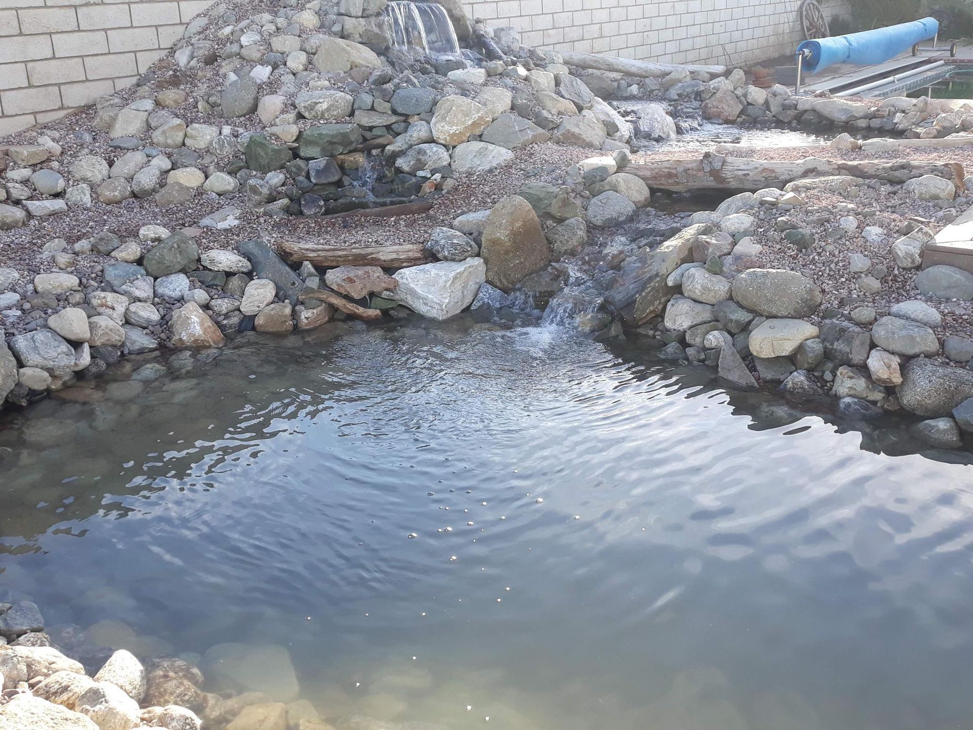 A small pond surrounded by rocks and a brick wall