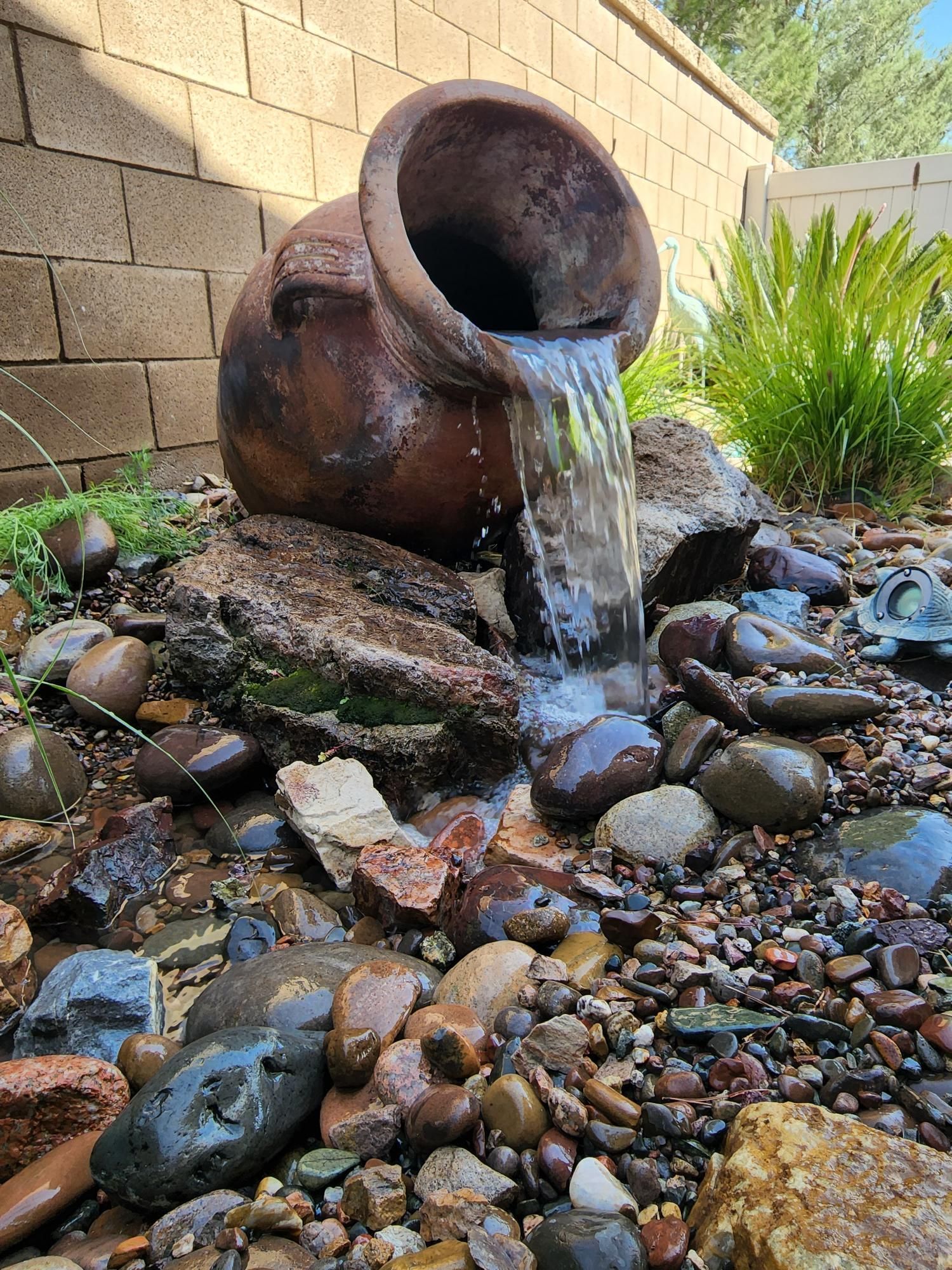 A waterfall is coming out of a pot in a rock garden.