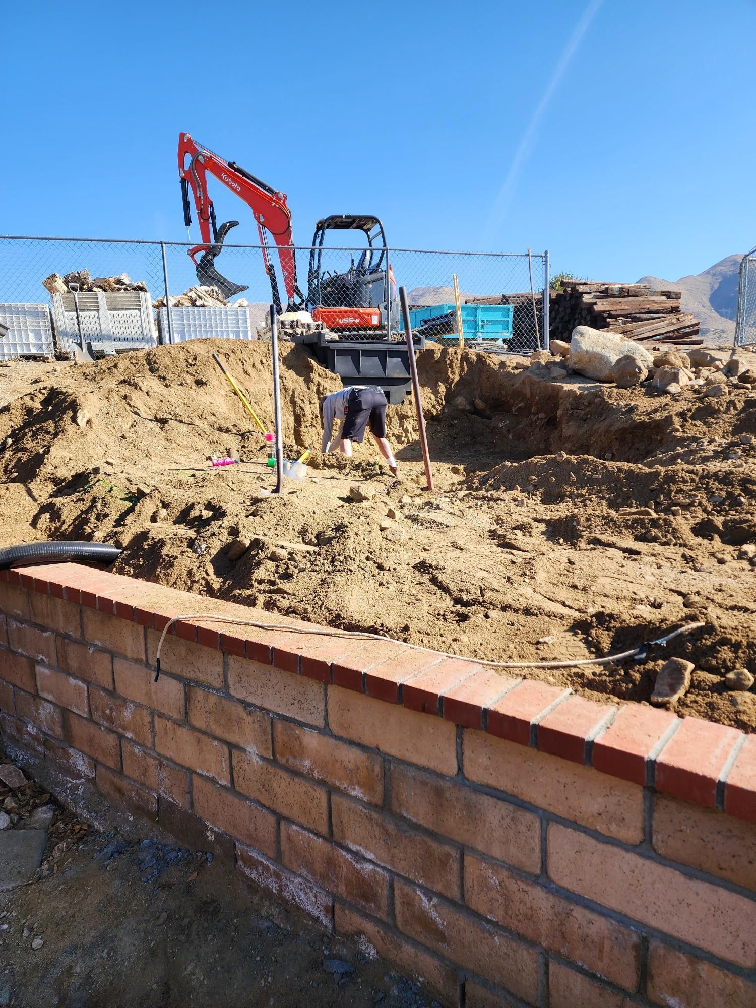 A construction site with a brick wall and an excavator in the background