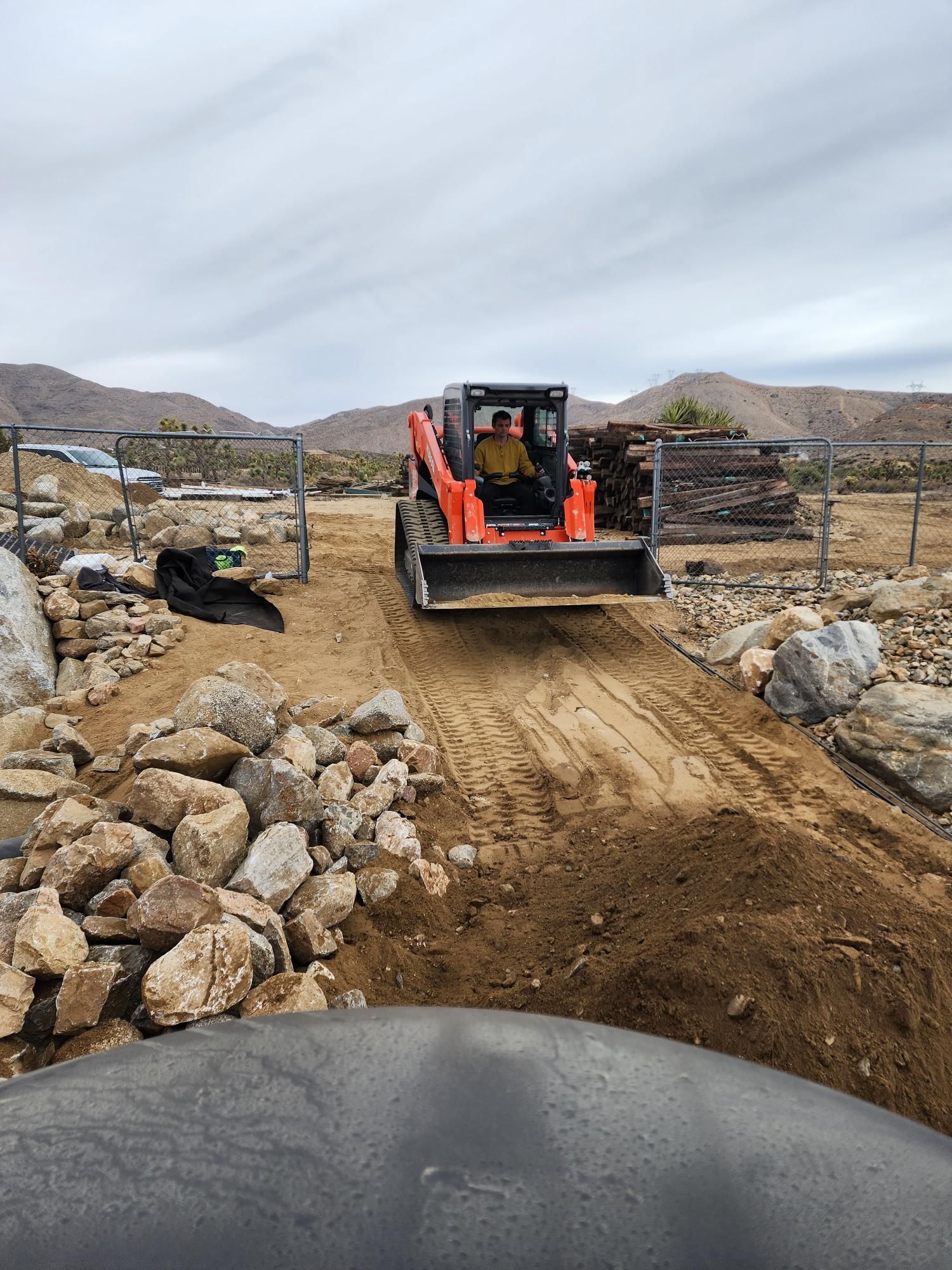 A bulldozer is driving down a dirt road next to a pile of rocks.