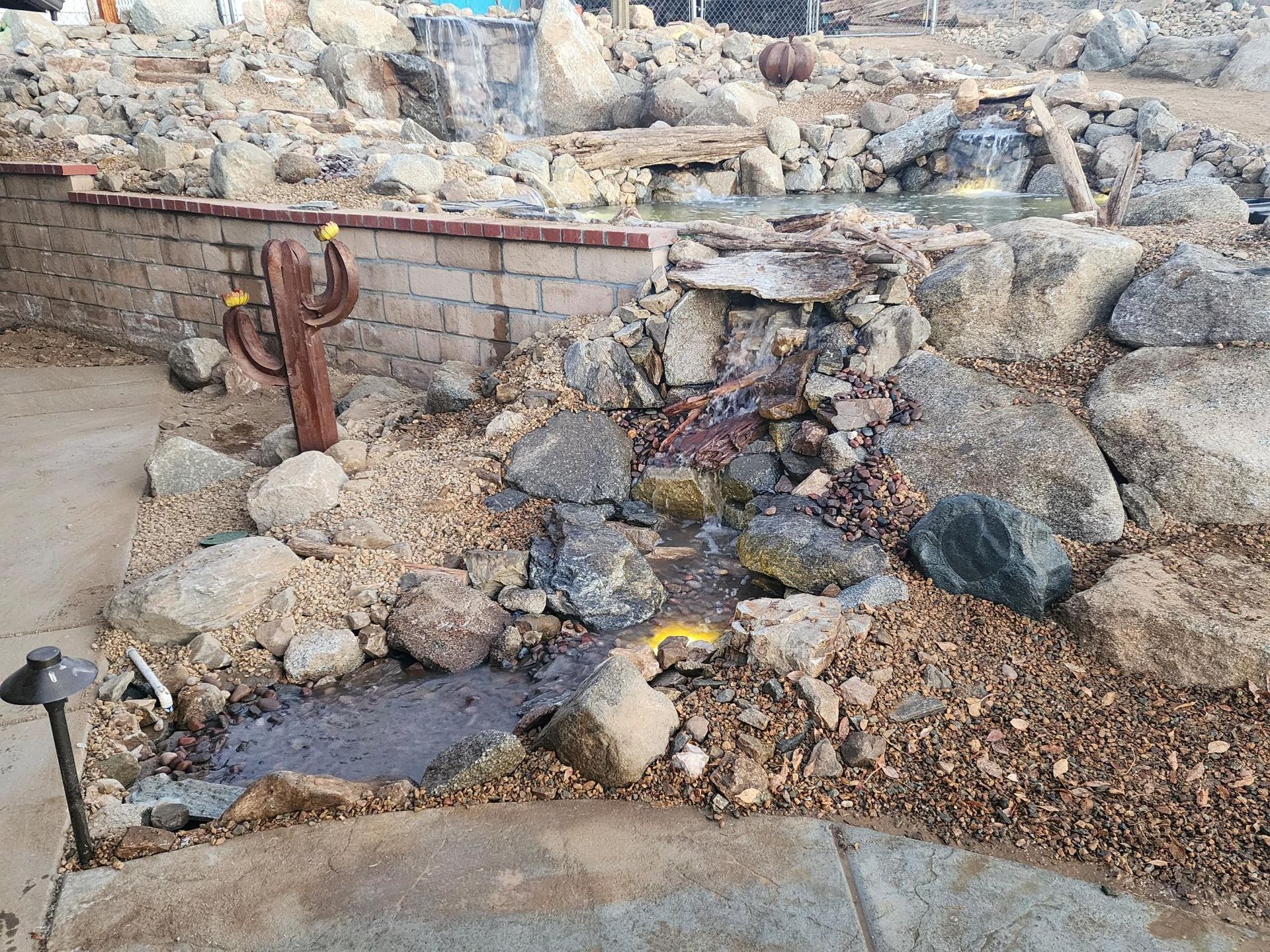 A small waterfall is surrounded by rocks and a brick wall.