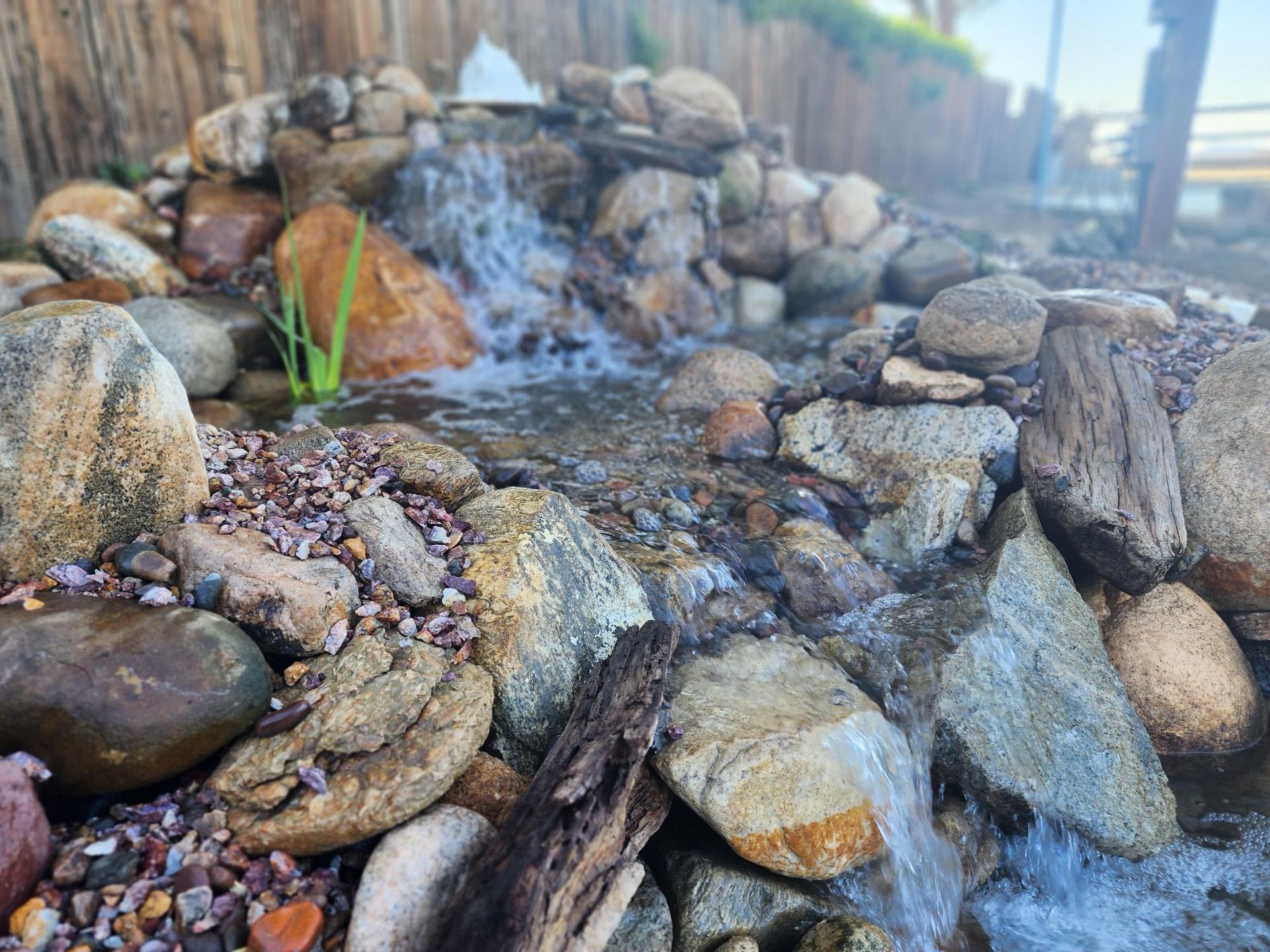 A waterfall is surrounded by rocks and a wooden fence.