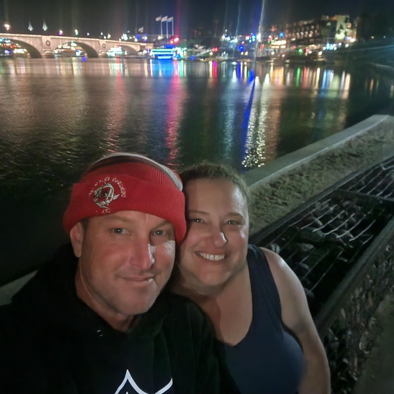 A man and a woman are posing for a picture in front of a body of water