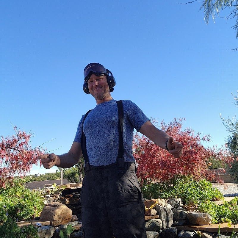 A man wearing headphones and suspenders is standing in a garden