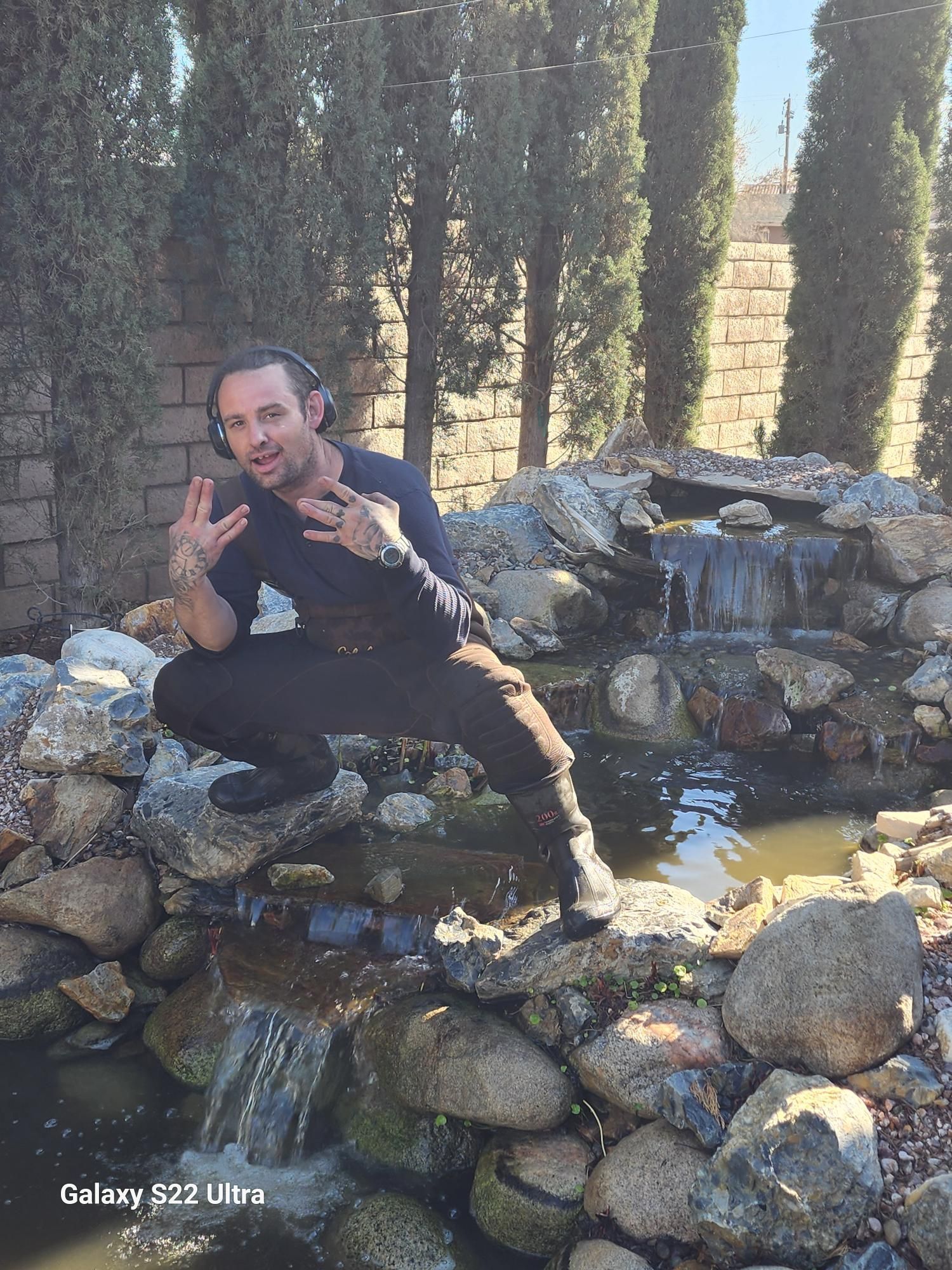 A man wearing headphones is sitting on a rock near a waterfall.