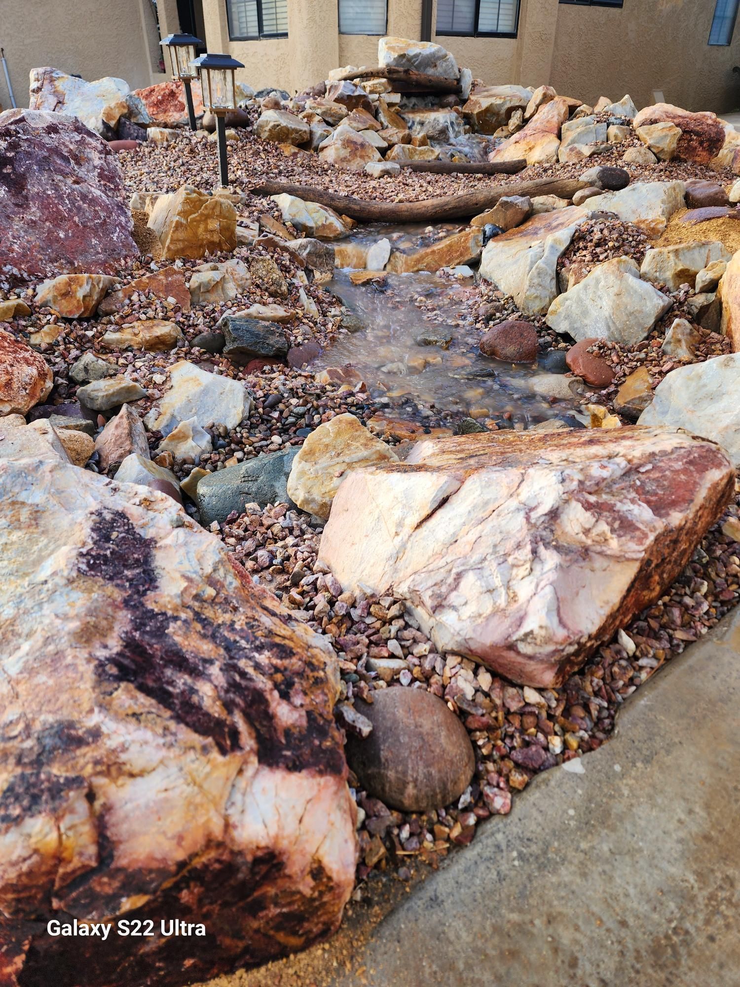 A pile of rocks and gravel in a garden with a house in the background.