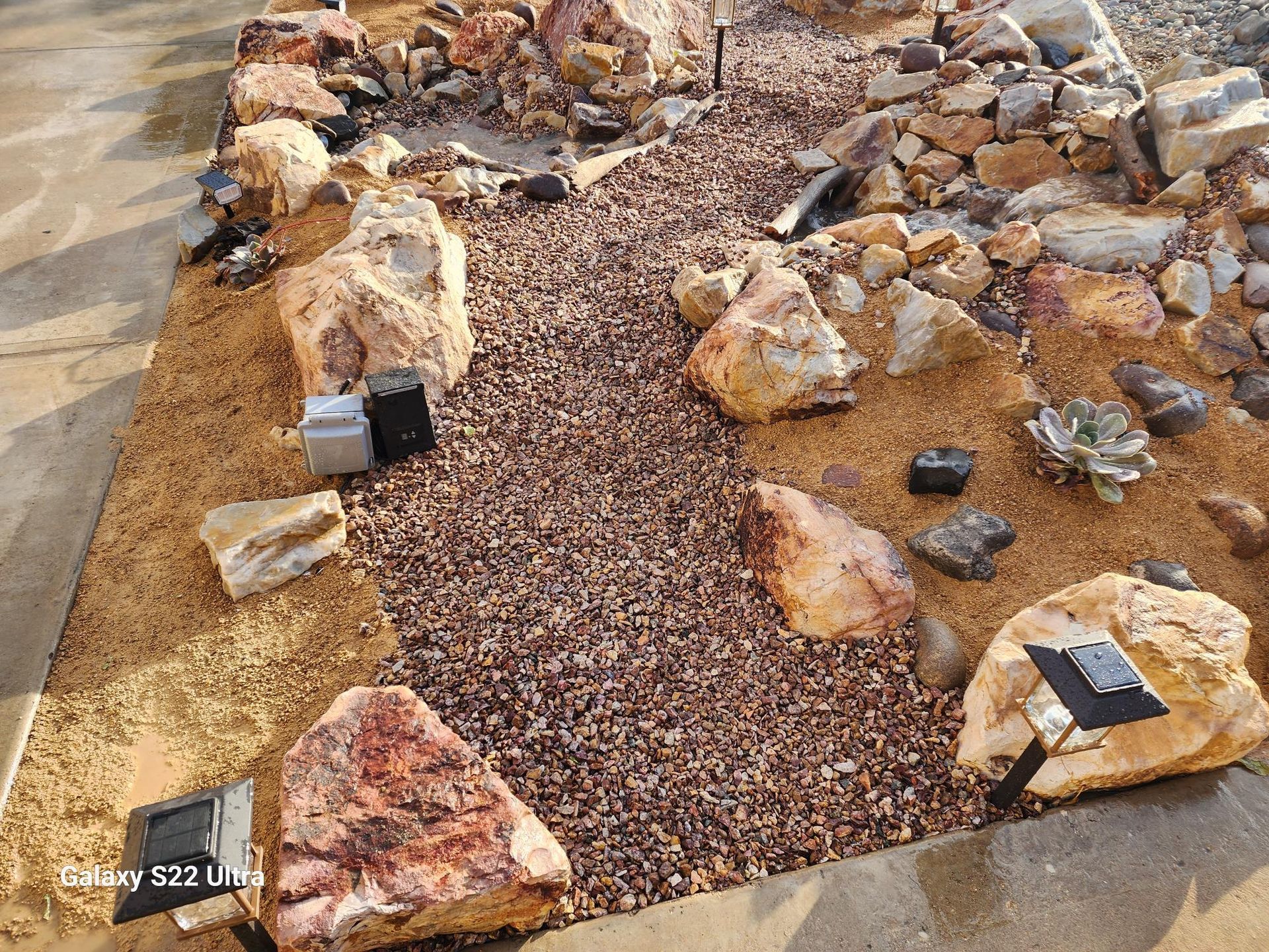 A path surrounded by rocks and gravel with solar lights.