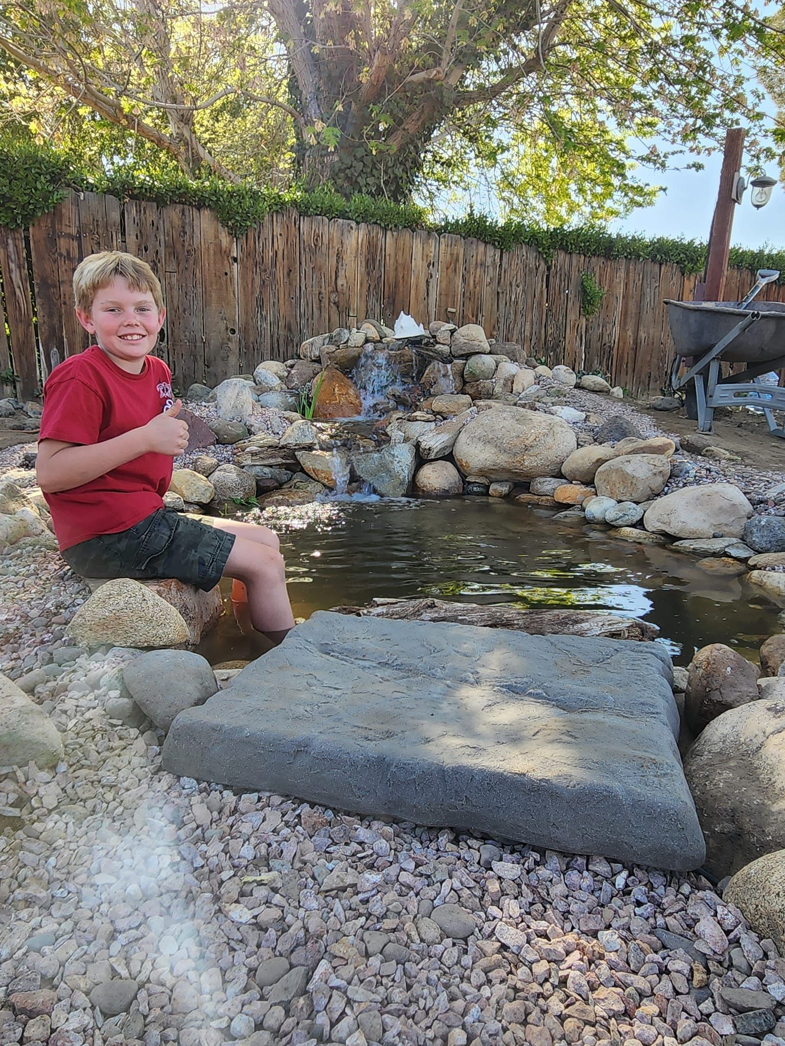 A young boy is sitting on a rock next to a pond.