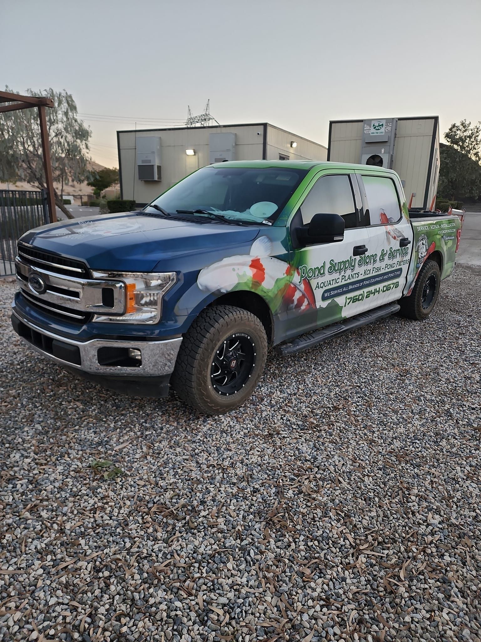 A blue and green truck is parked in a gravel lot.