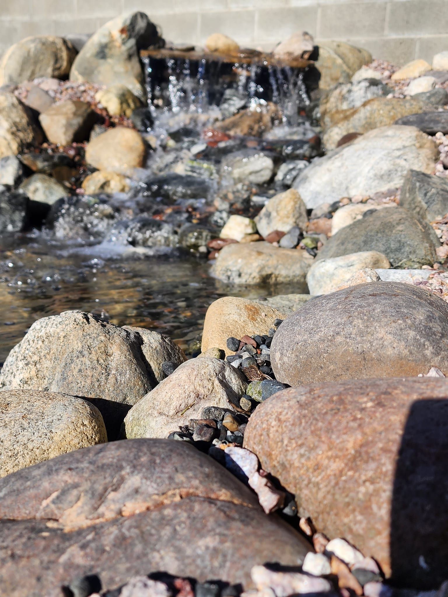 A waterfall is surrounded by rocks and a brick wall.