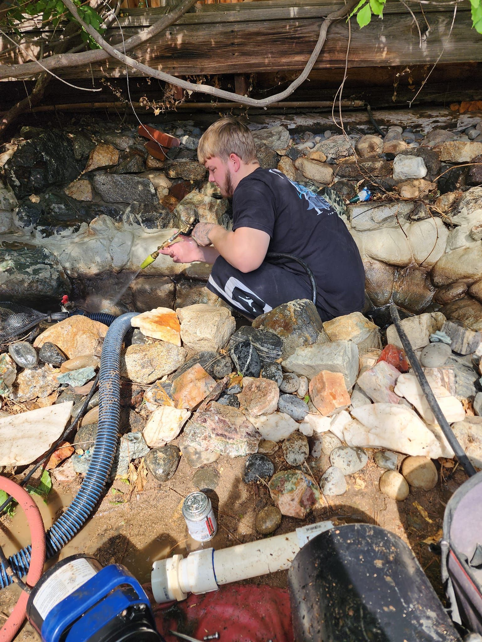 A man is kneeling on a pile of rocks working on a pipe.