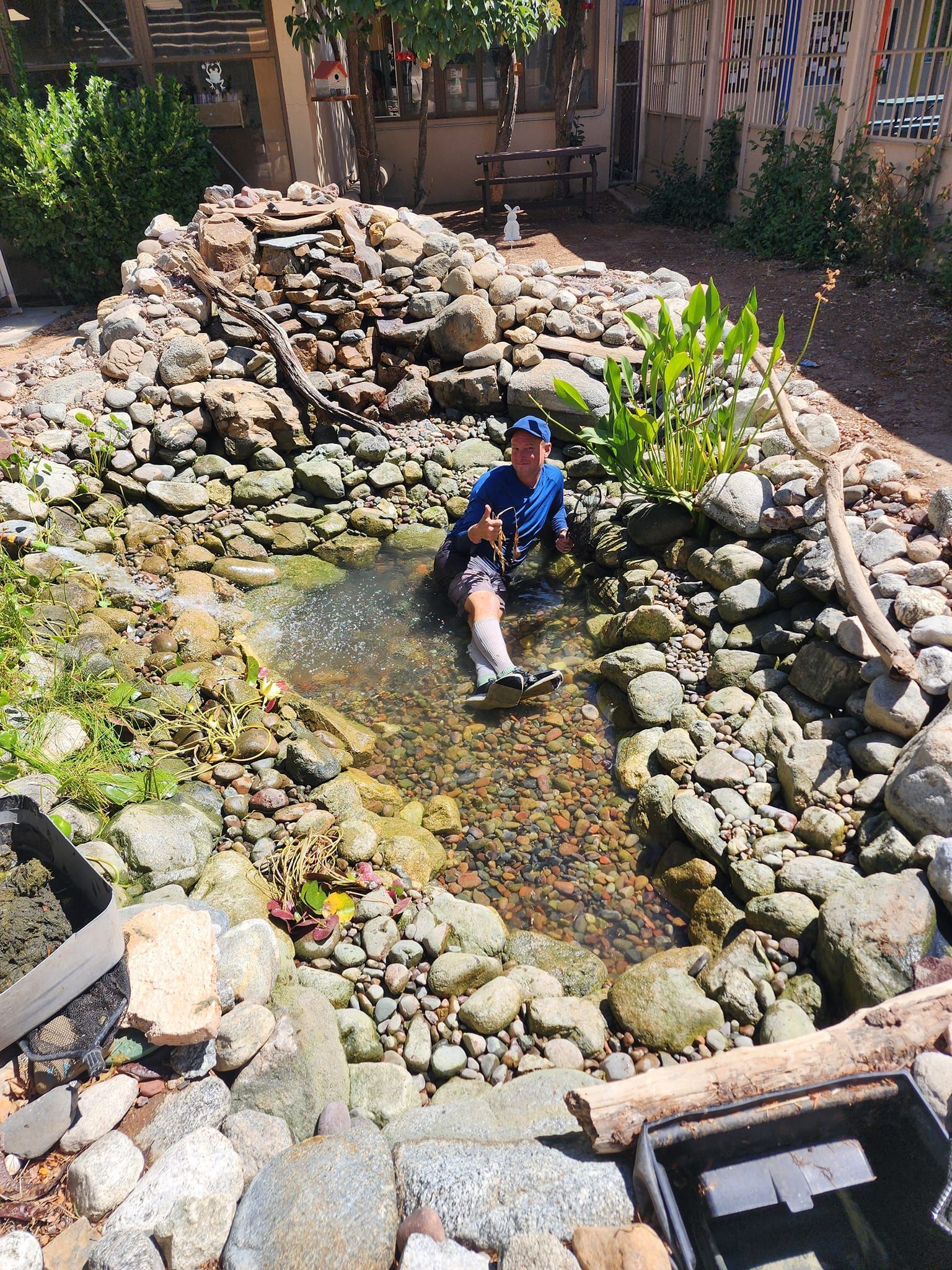A man is sitting in a pond surrounded by rocks.
