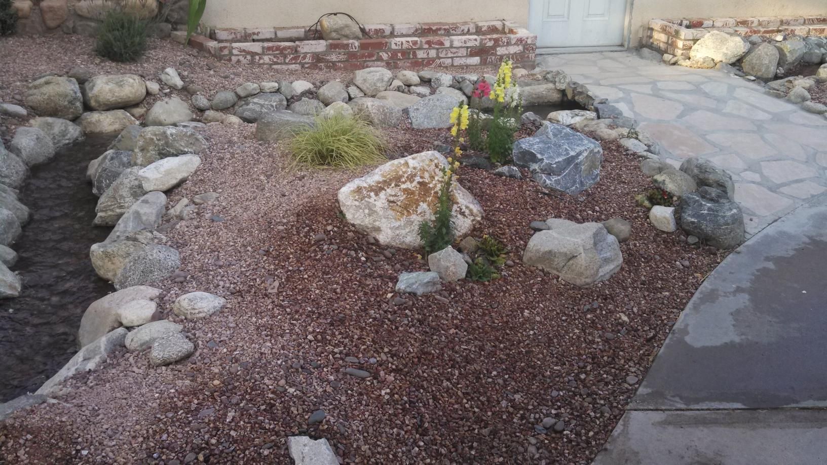 A rock garden with flowers and rocks in front of a house.