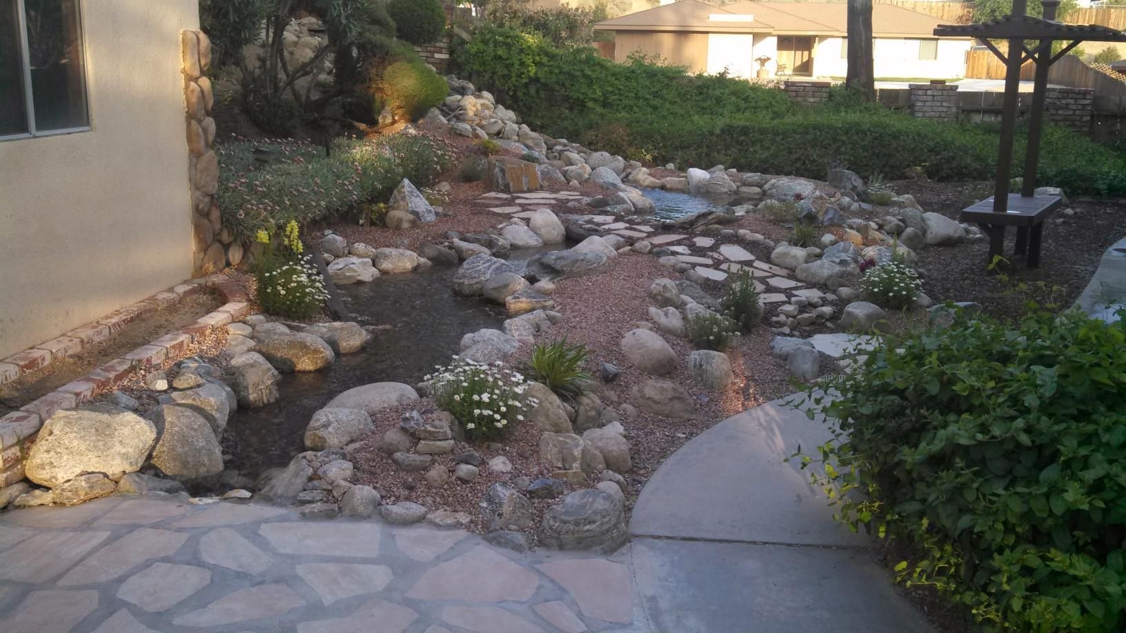 A stone walkway leading to a stream surrounded by rocks and bushes