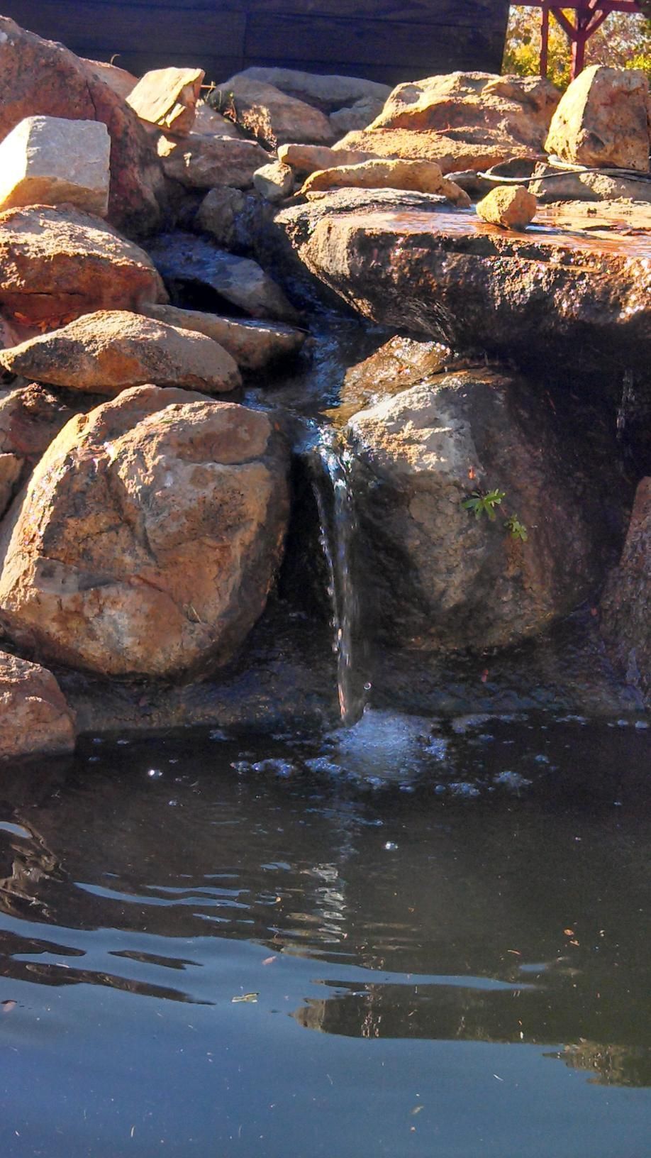 A small waterfall is surrounded by rocks in a pond.
