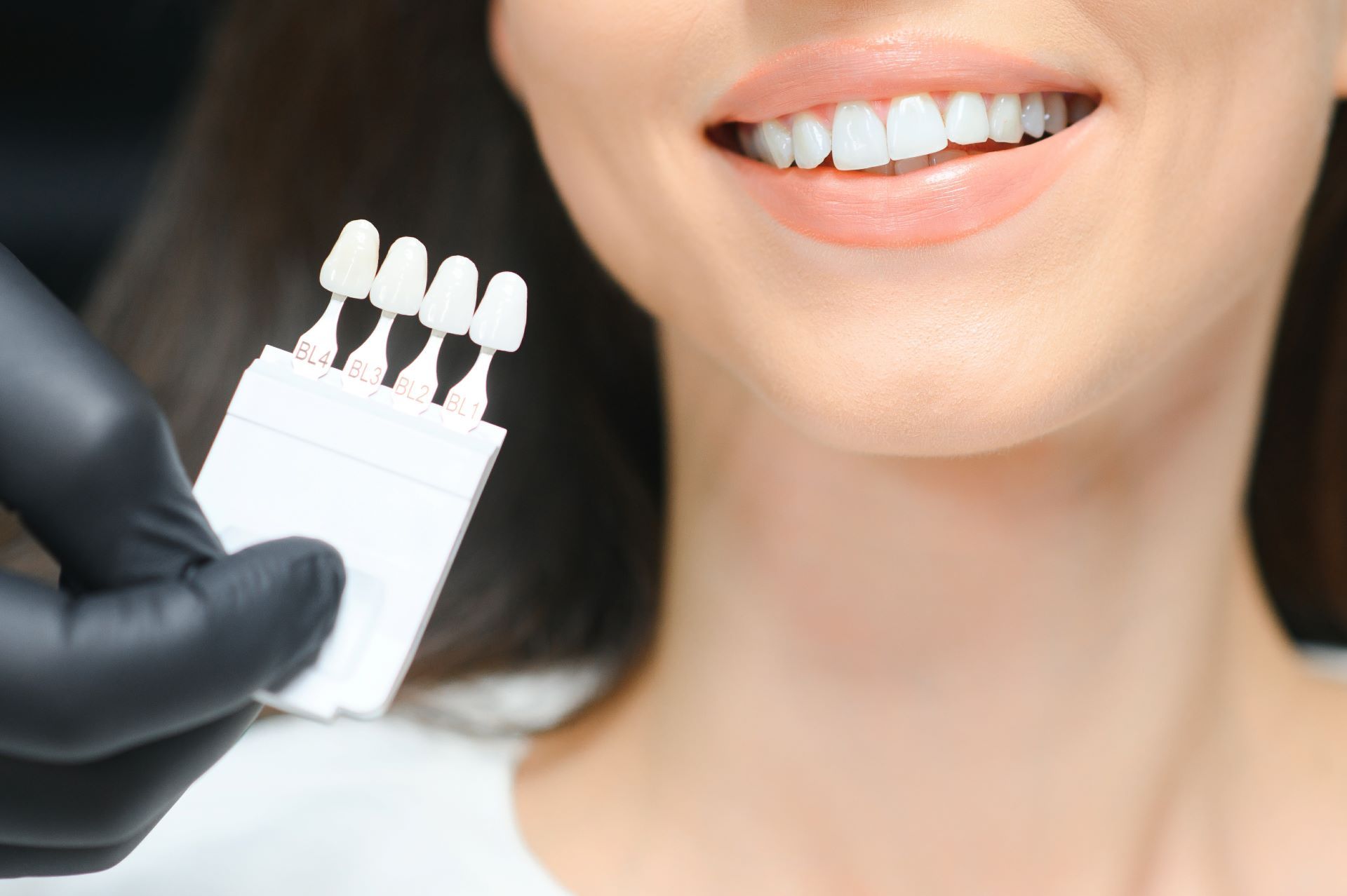 A dentist holding a tooth shade guide next to a smiling patient's teeth.