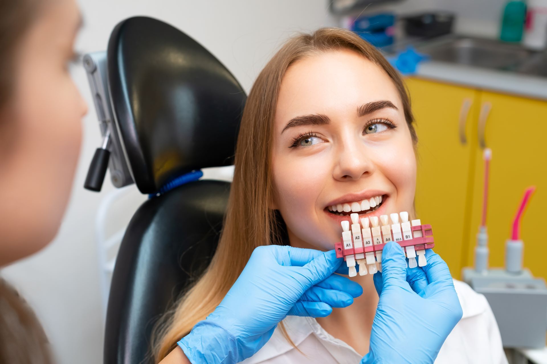 A woman is sitting in a dental chair while a dentist holds a model of her teeth.