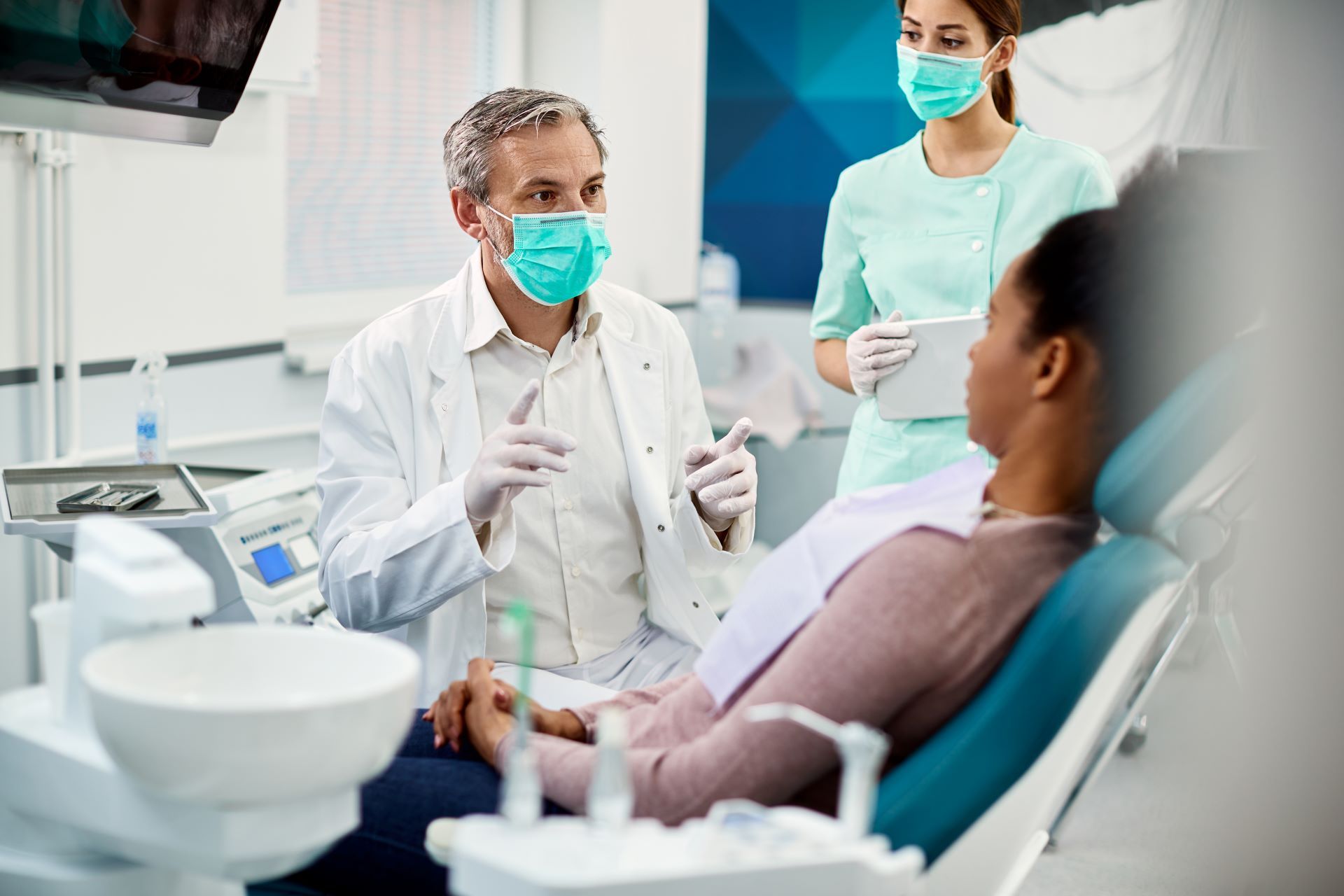 A dentist wearing a mask is talking to a patient in a dental chair.