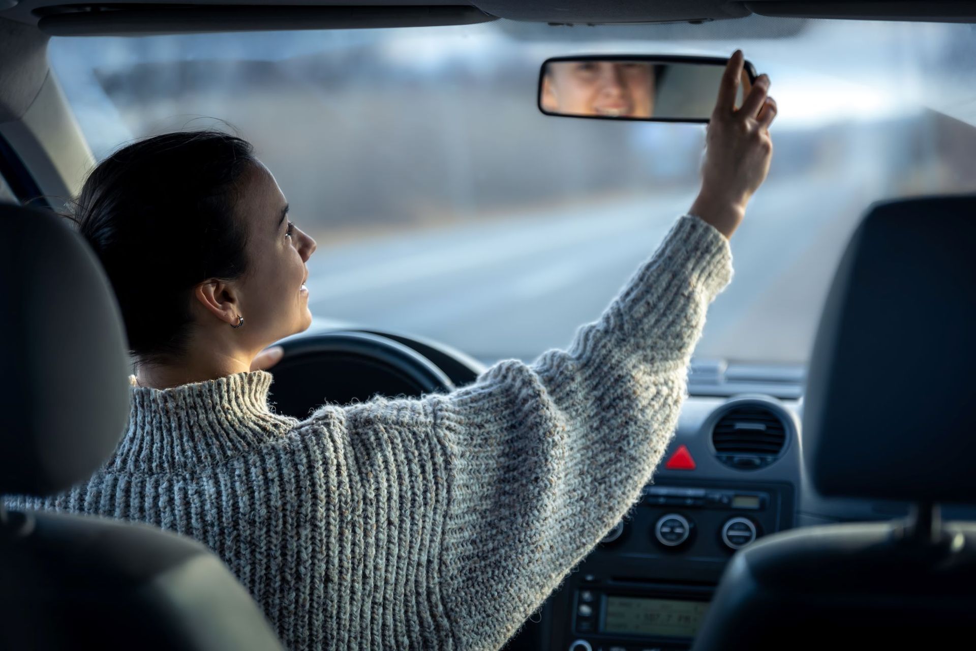 woman smiling, checking rearview mirror inside car