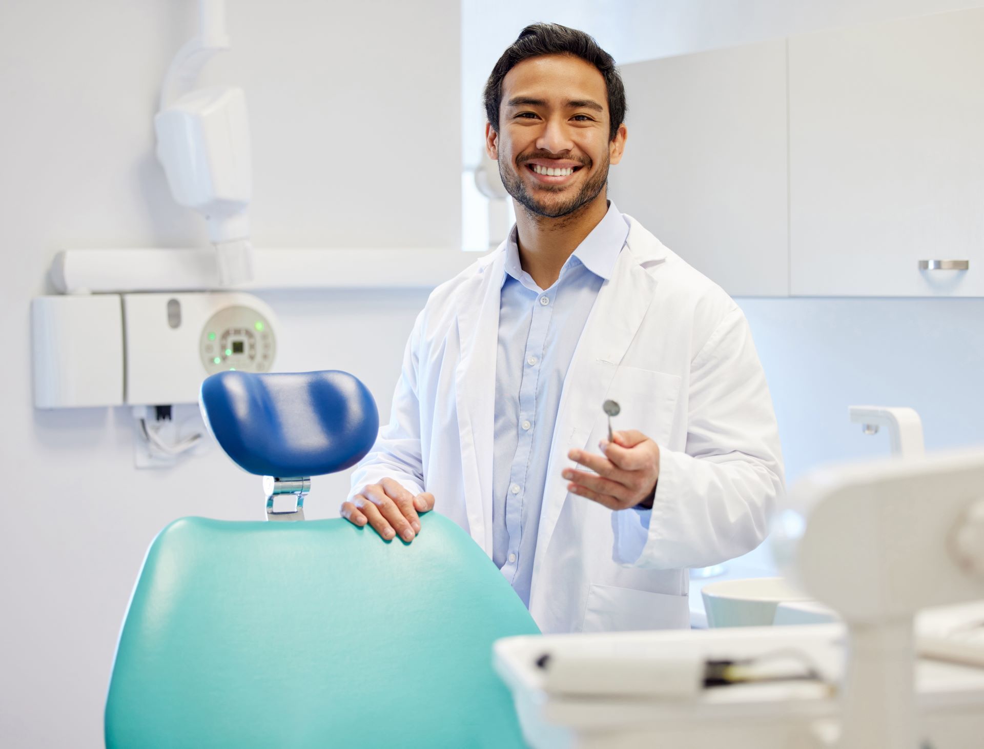 A dentist is standing next to a dental chair in a dental office.