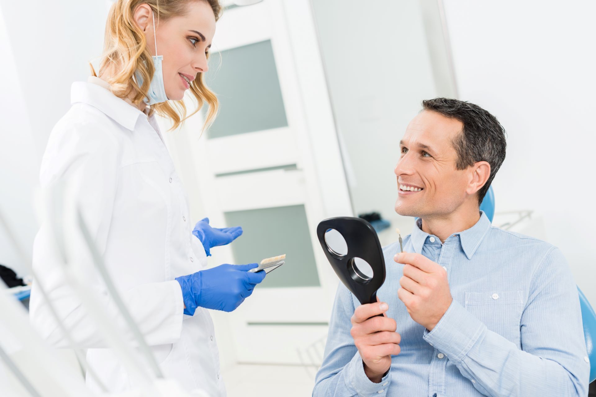 Male patient choosing tooth implant in modern dental clinic while female dentist holds samples of implants