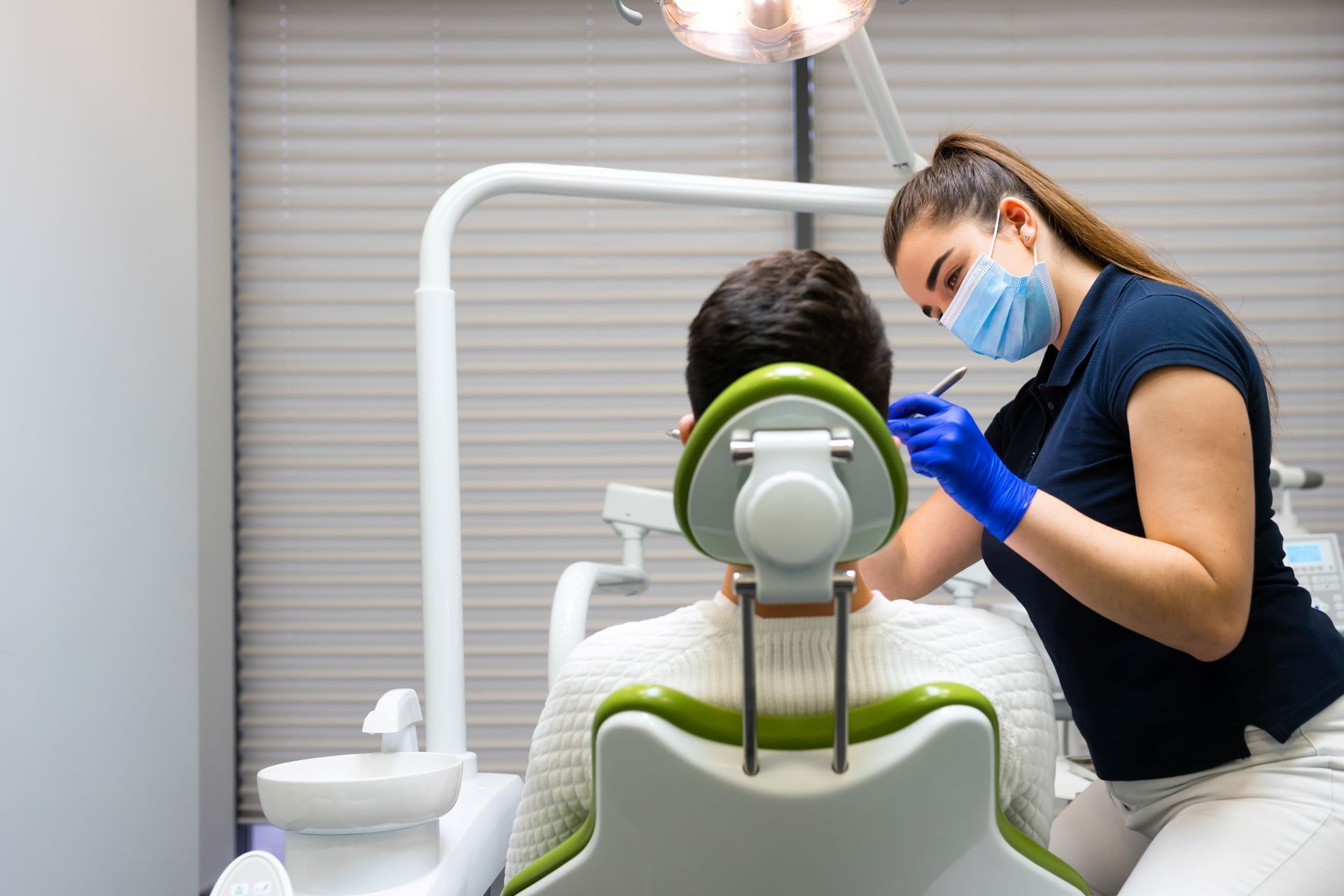 Man at dental check-up in chair with back towards us, while woman dental professional examines teeth