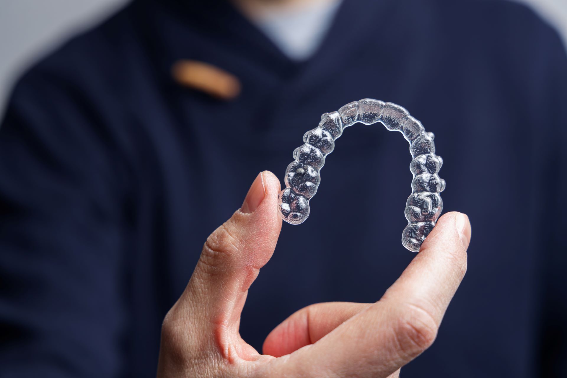 close up of man holding an Invisalign with two fingers. Navy shirt blurred in background.