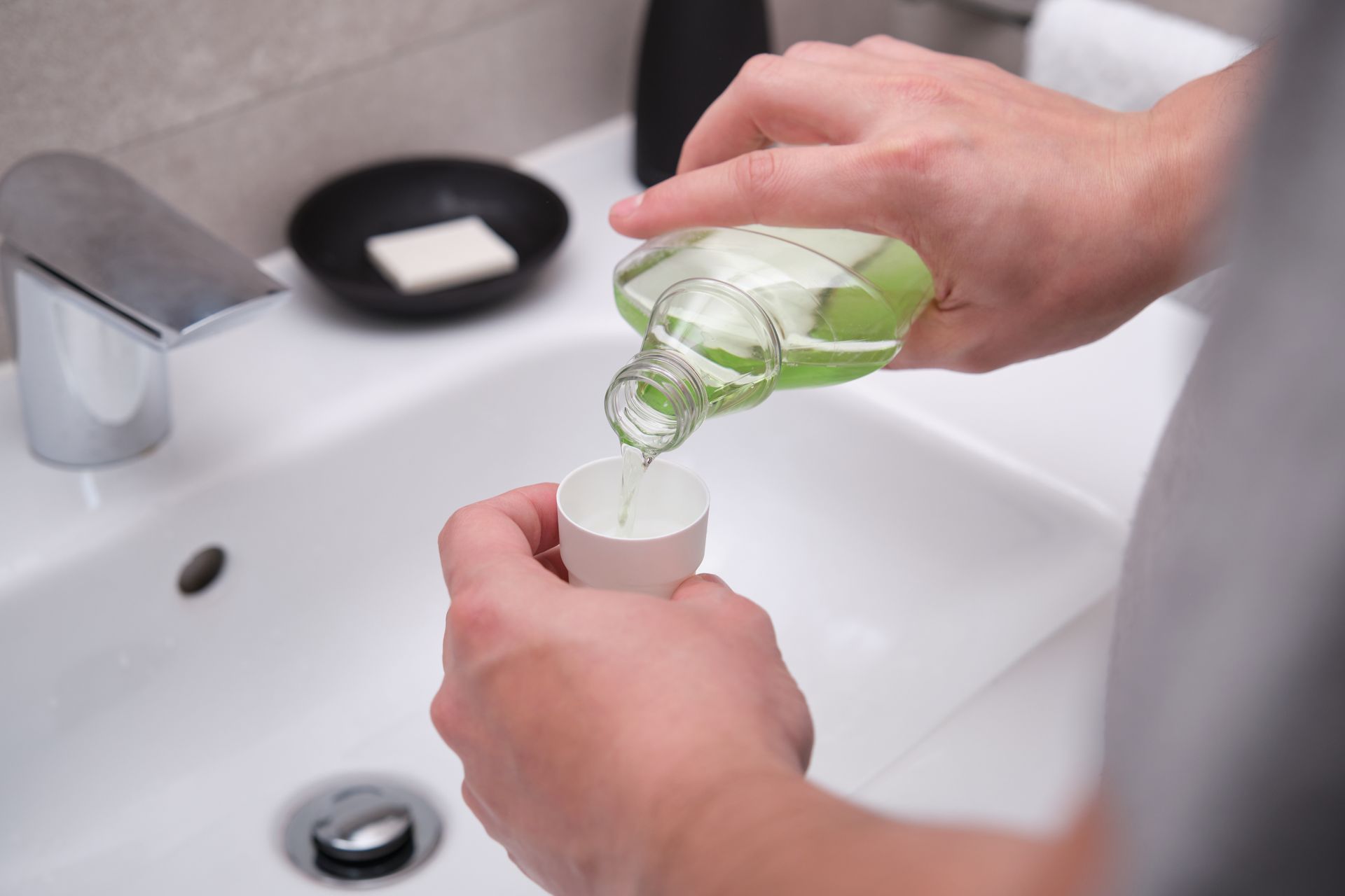 Man pouring green mouthwash from bottle into cap in bathroom