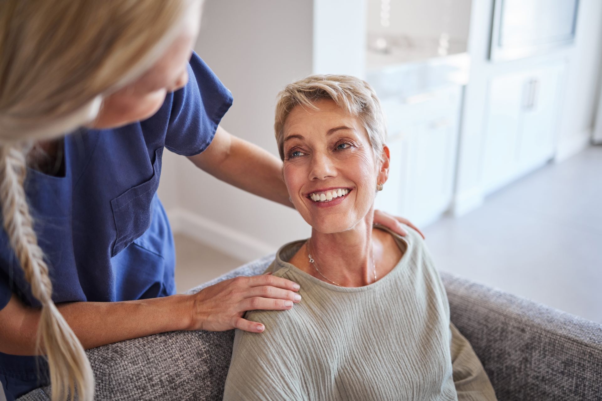 elderly woman sitting in waiting room, looking up and smiling at nurse