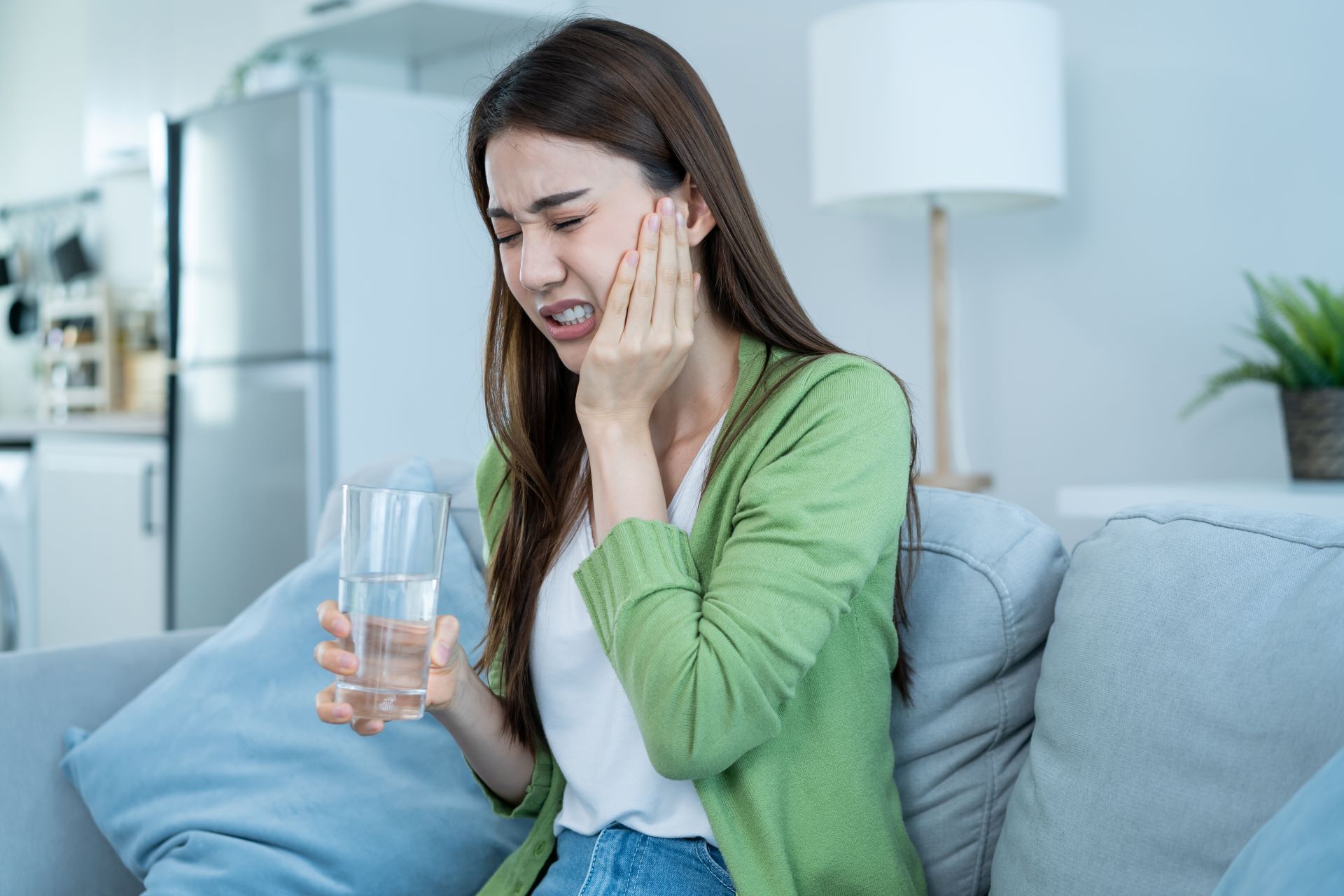 A woman is sitting on a couch holding a glass of water.