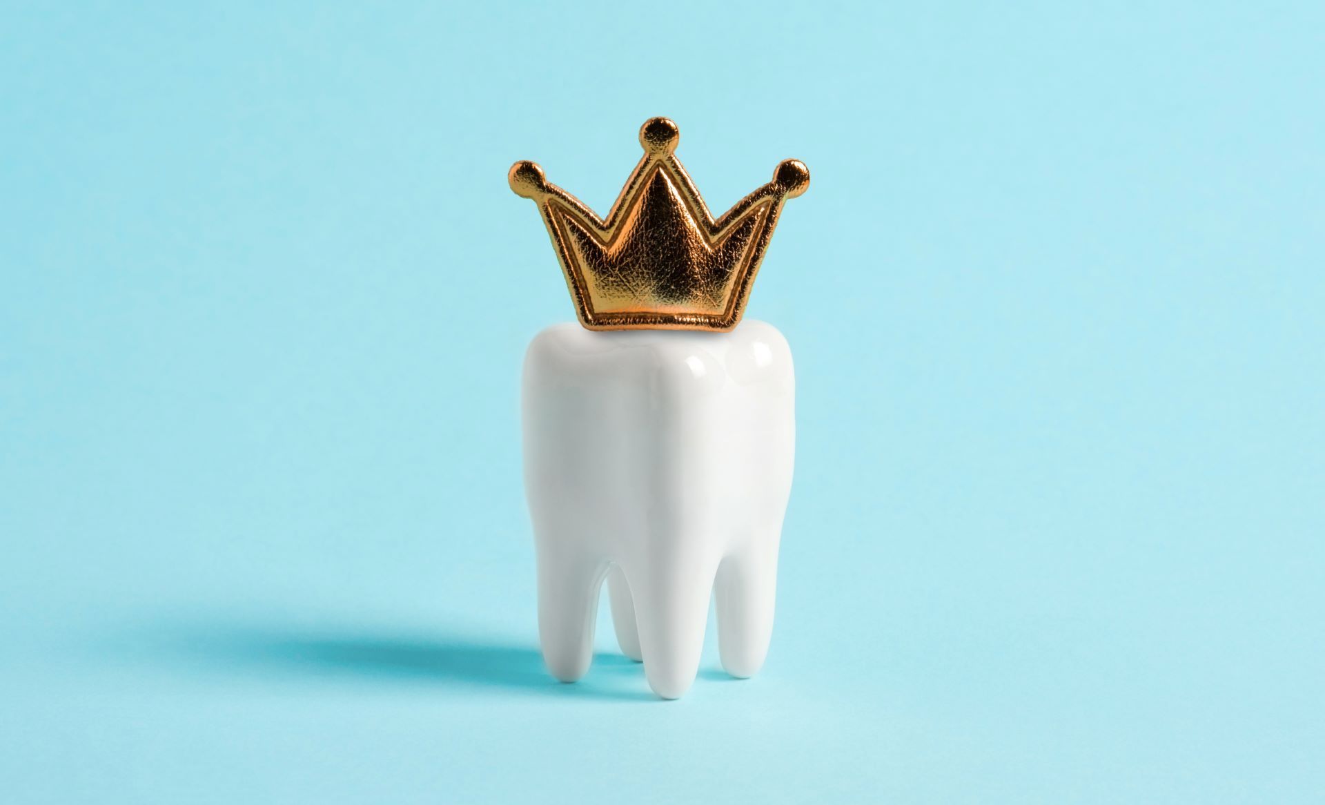 A white tooth with a gold crown on it on a blue background.