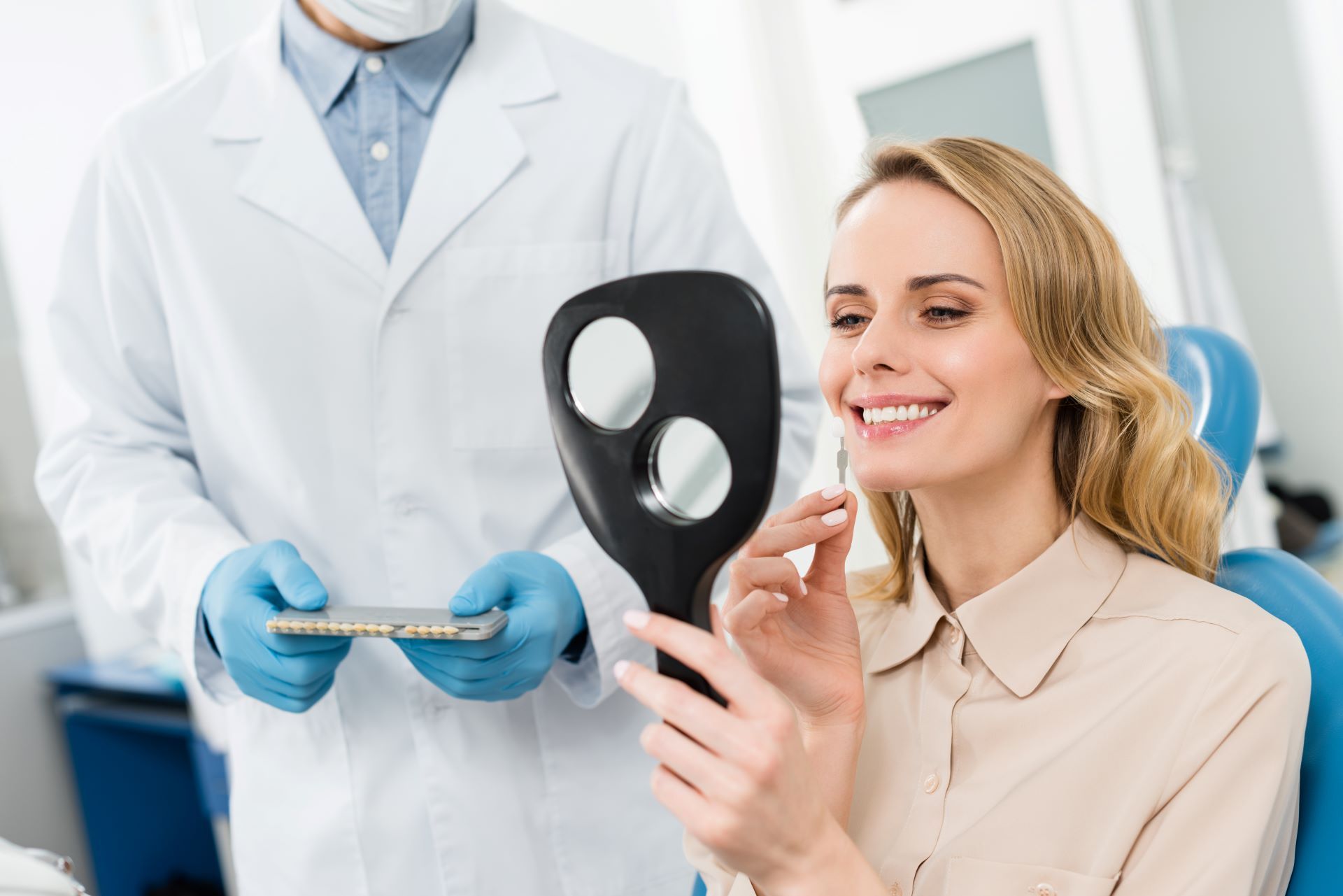 woman looking at tooth implants and smiling while dentist holds tray of other options