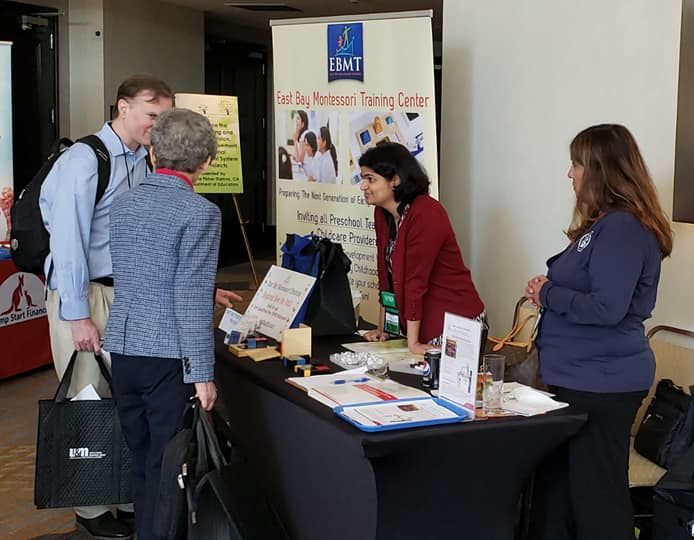 A group of people standing around a table in front of a sign that says ermt
