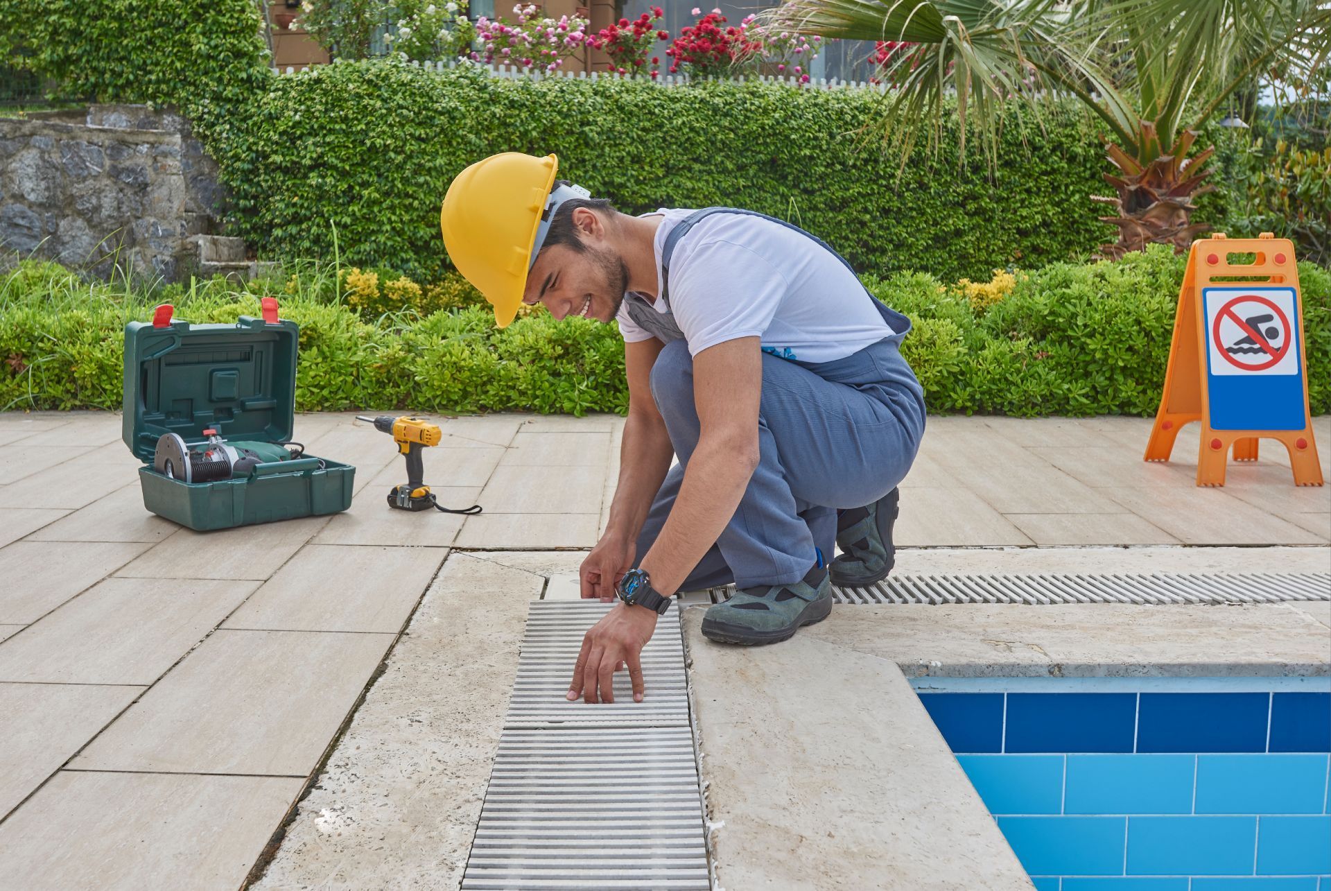 A man is working on a drain on the side of a swimming pool.