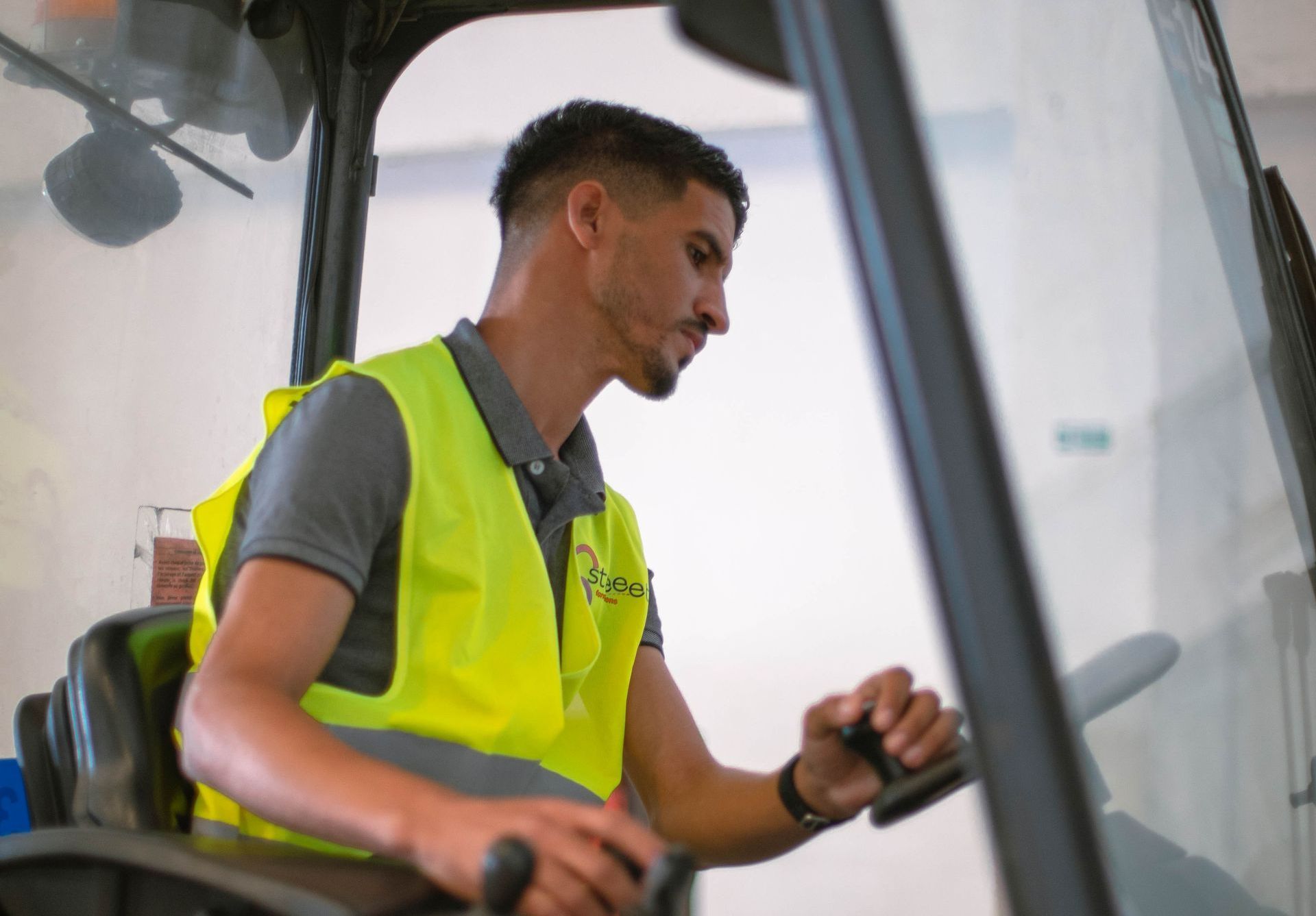 Un homme portant un gilet orange se tient debout dans un entrepôt, les bras croisés.