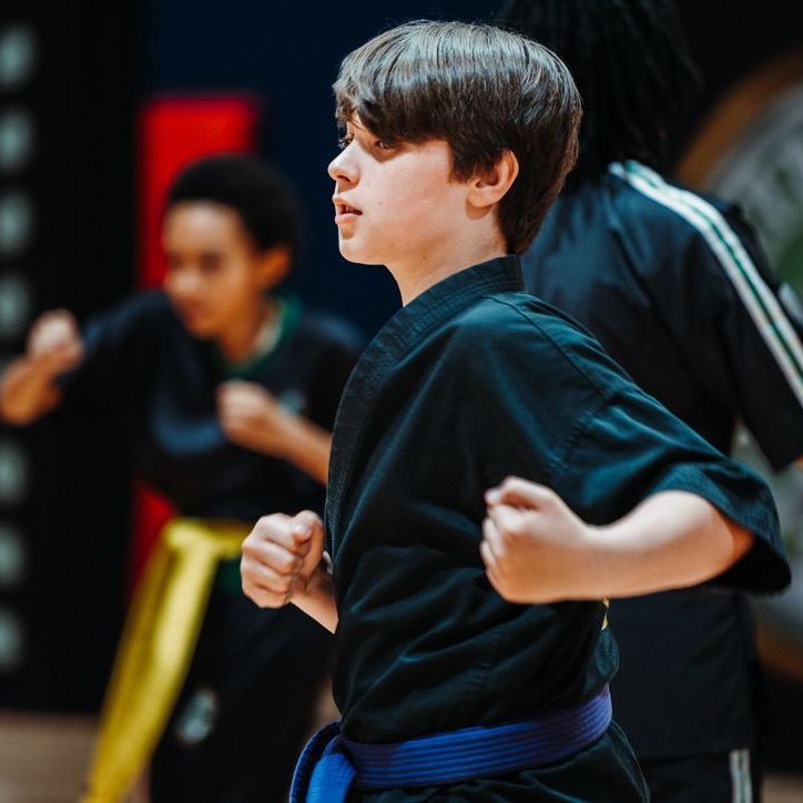 A man is kneeling down next to a young boy in a taekwondo class.