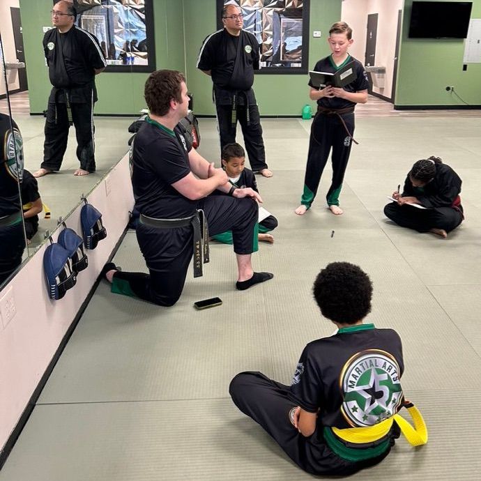 A group of children are practicing karate with a teacher in a gym.