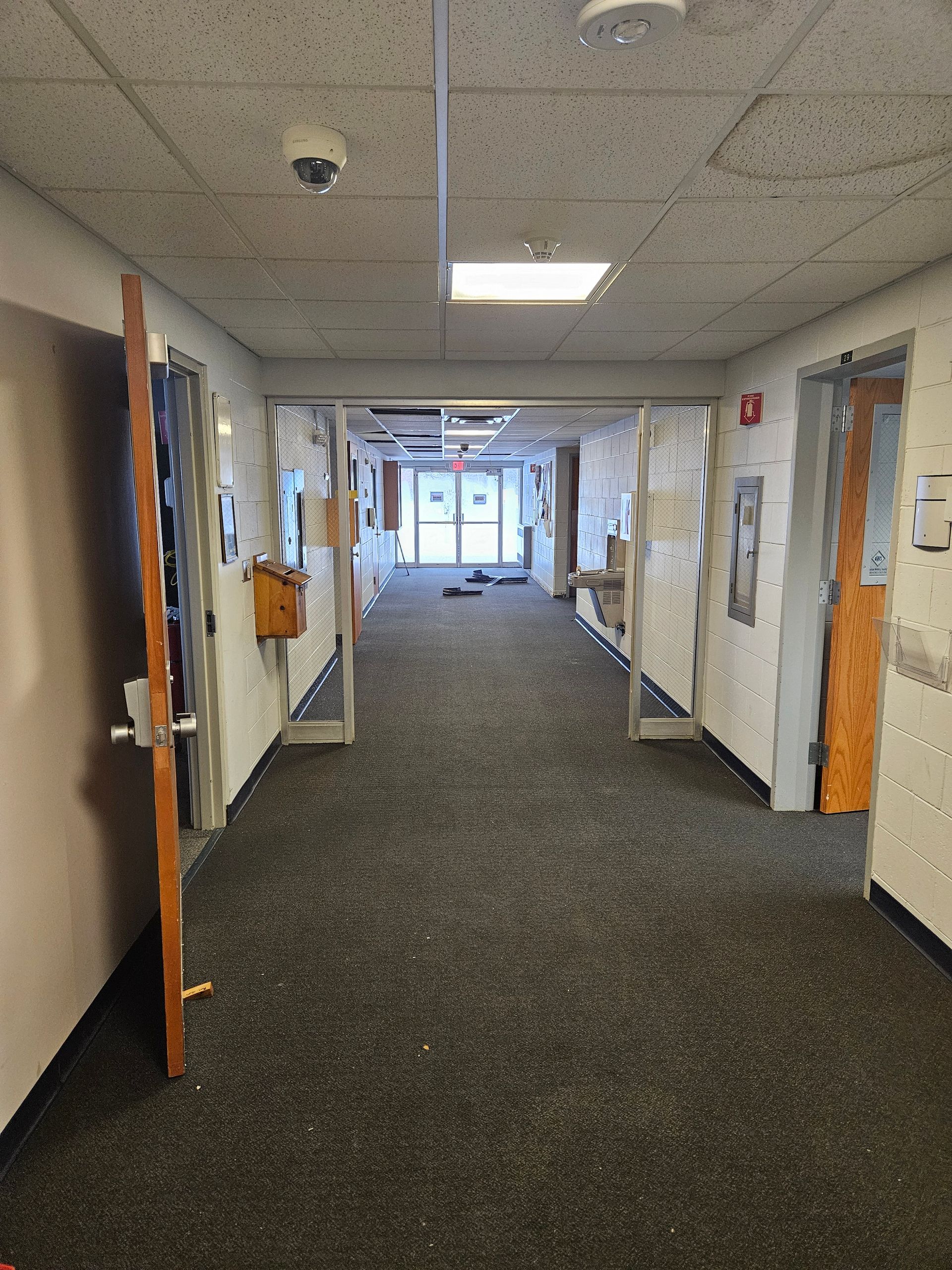 A long hallway with a lot of doors and a fire alarm on the ceiling.