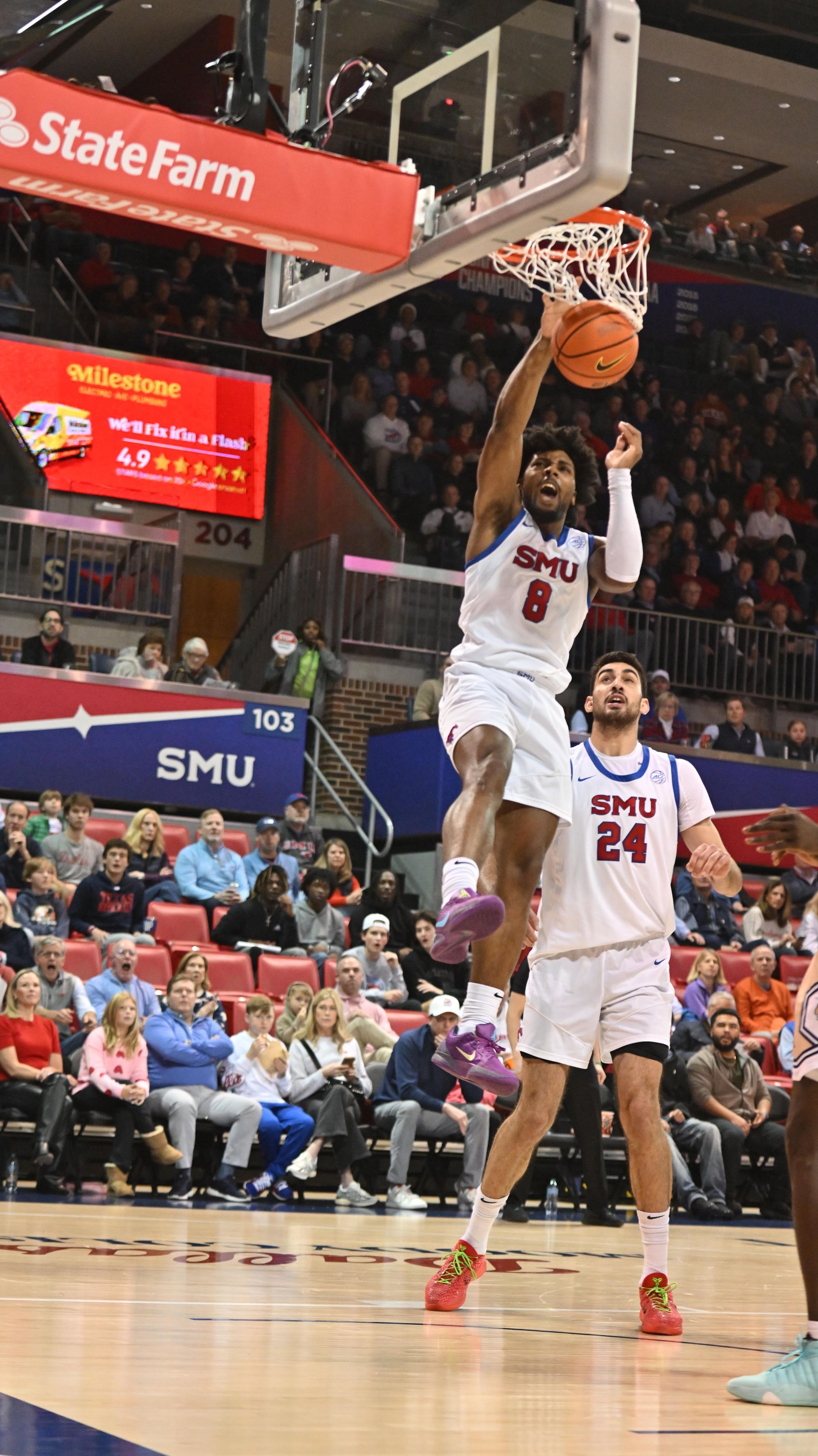 Basketball player in white SMU uniform dunks during a game, crowd and StateFarm sign in background