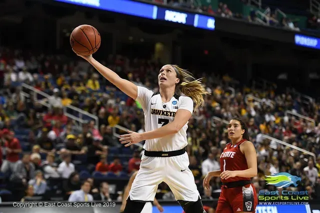 Basketball player in black and white uniform shoots the ball in a crowded arena.