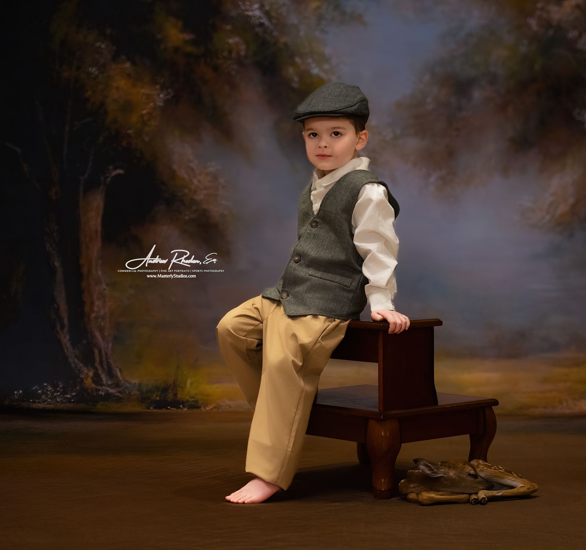 Young boy in vest and cap, sitting on a step stool against a misty forest backdrop.