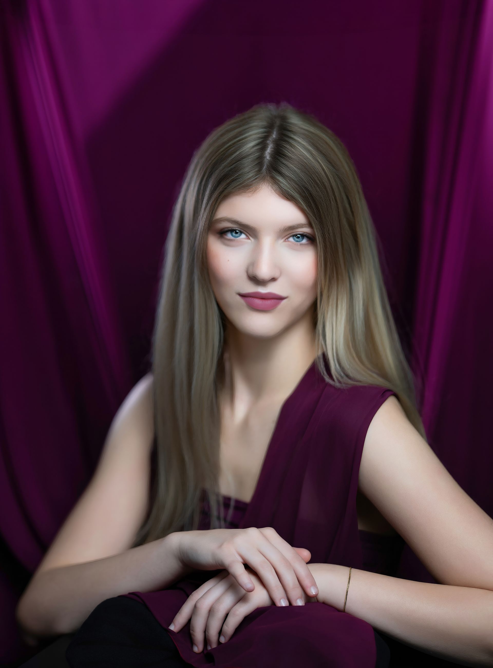 Portrait of a woman with long blonde hair in a burgundy dress against a purple draped backdrop