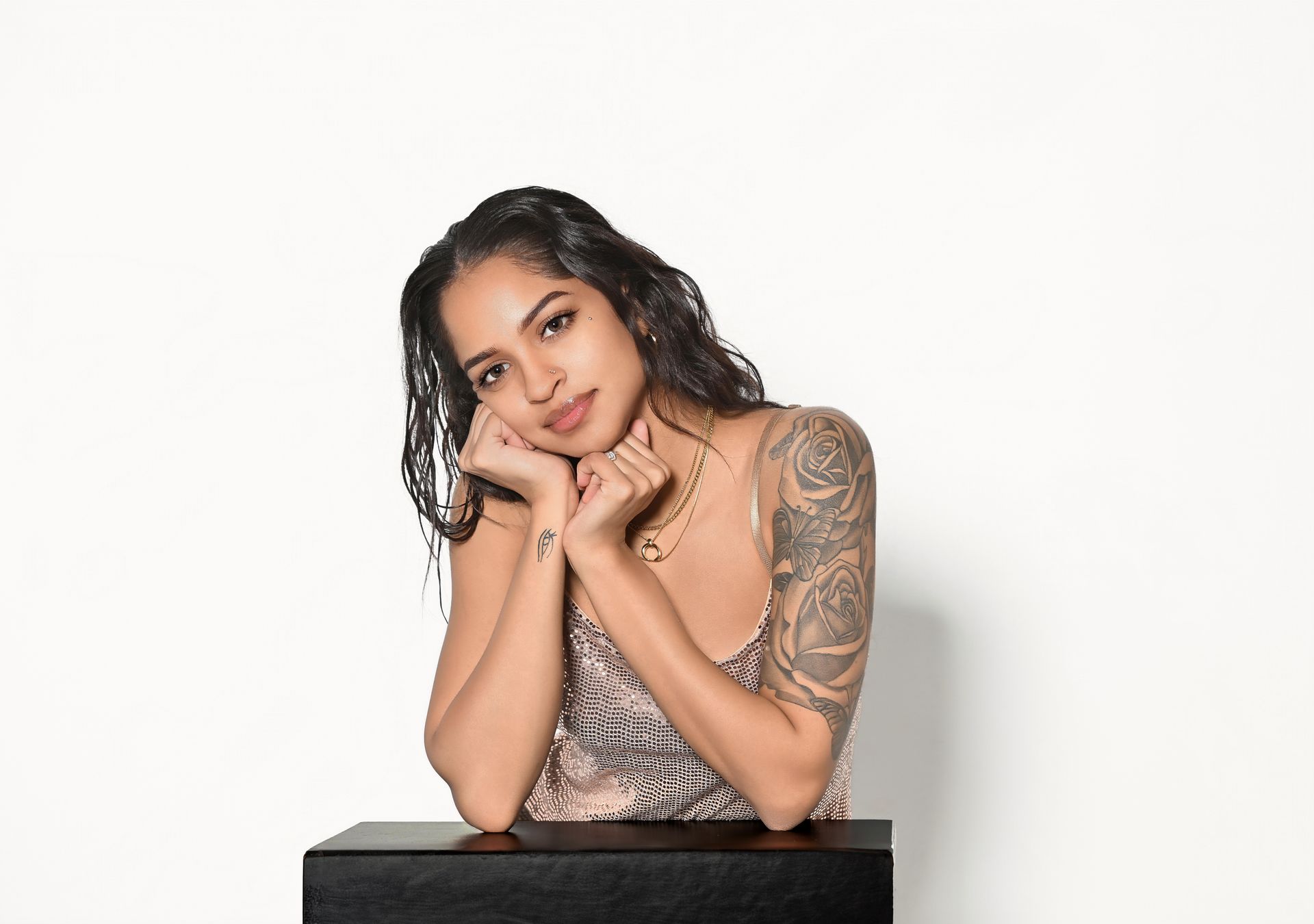 Woman in a black sequined outfit posing on a stool against a dark background.