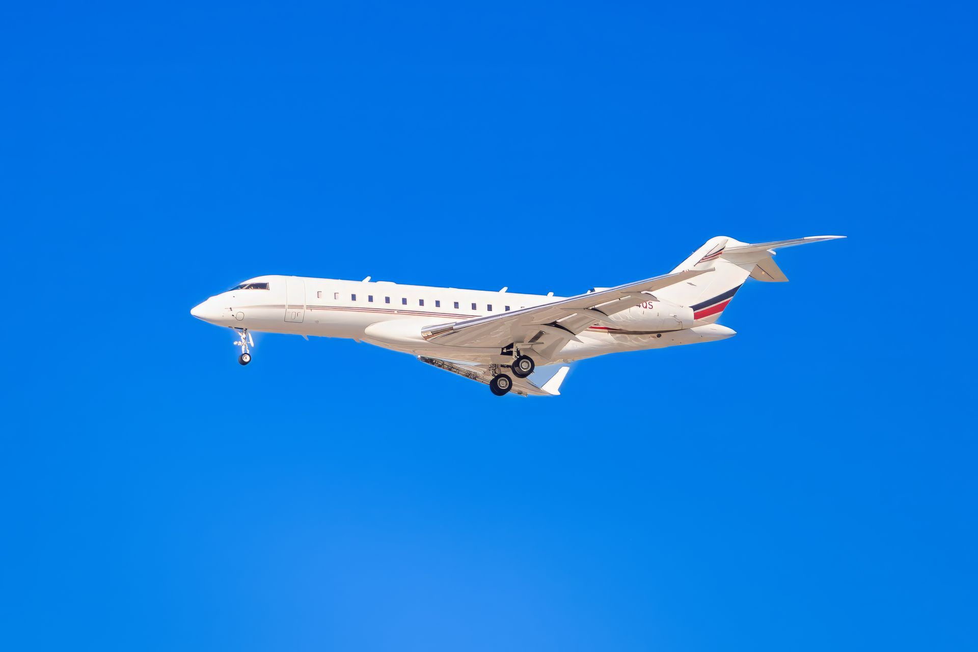 White airplane in flight against a bright blue sky, landing gear deployed.