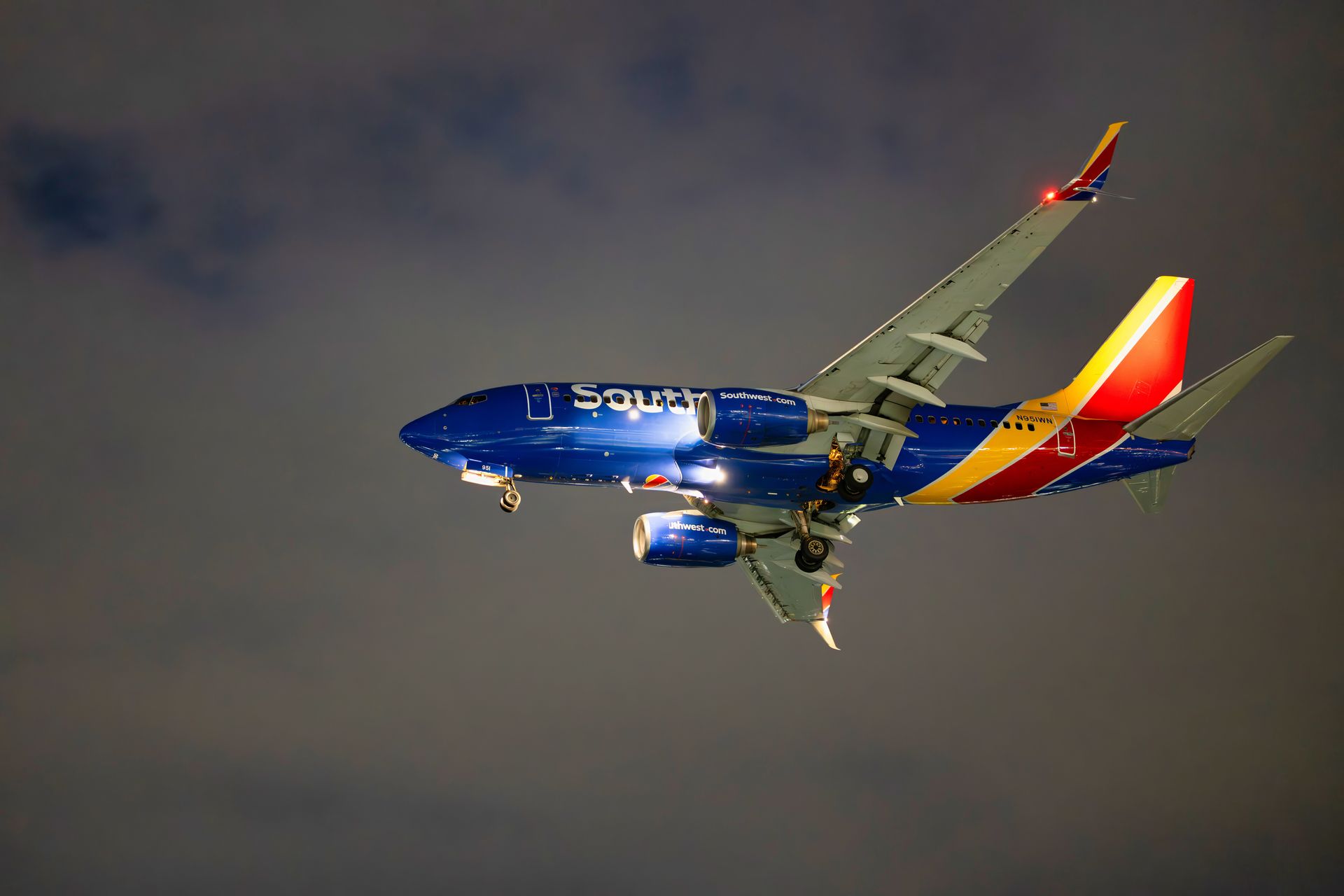 Southwest Airlines plane in flight, blue fuselage, multi-colored wing and tail, descending in a cloudy sky.