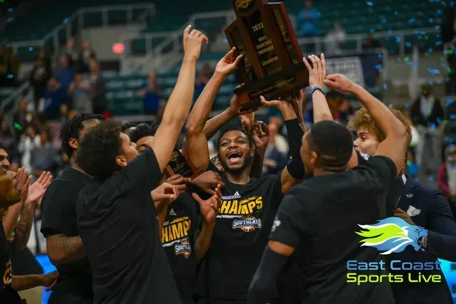 Basketball team in black jerseys celebrating while raising a trophy on the court