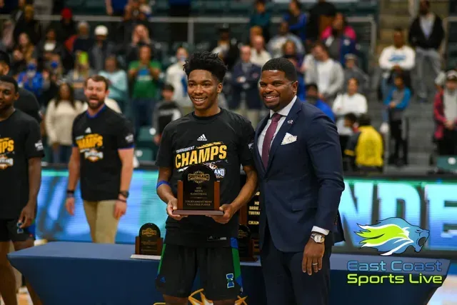 Basketball player holding a CHAMPS trophy beside a suited man on court after a game
