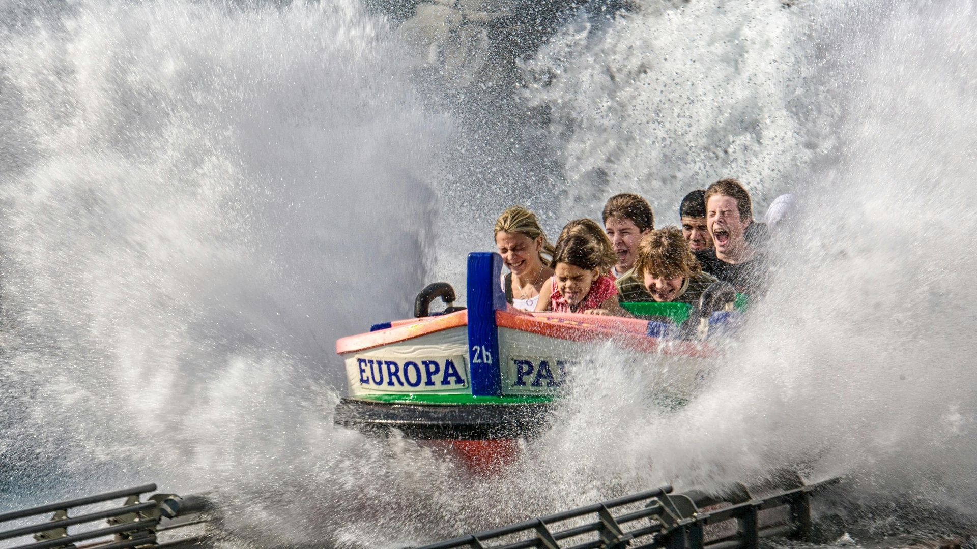 People on a water ride at Europa-Park get splashed. A boat with passengers plunges into a wall of water, spraying everyone.