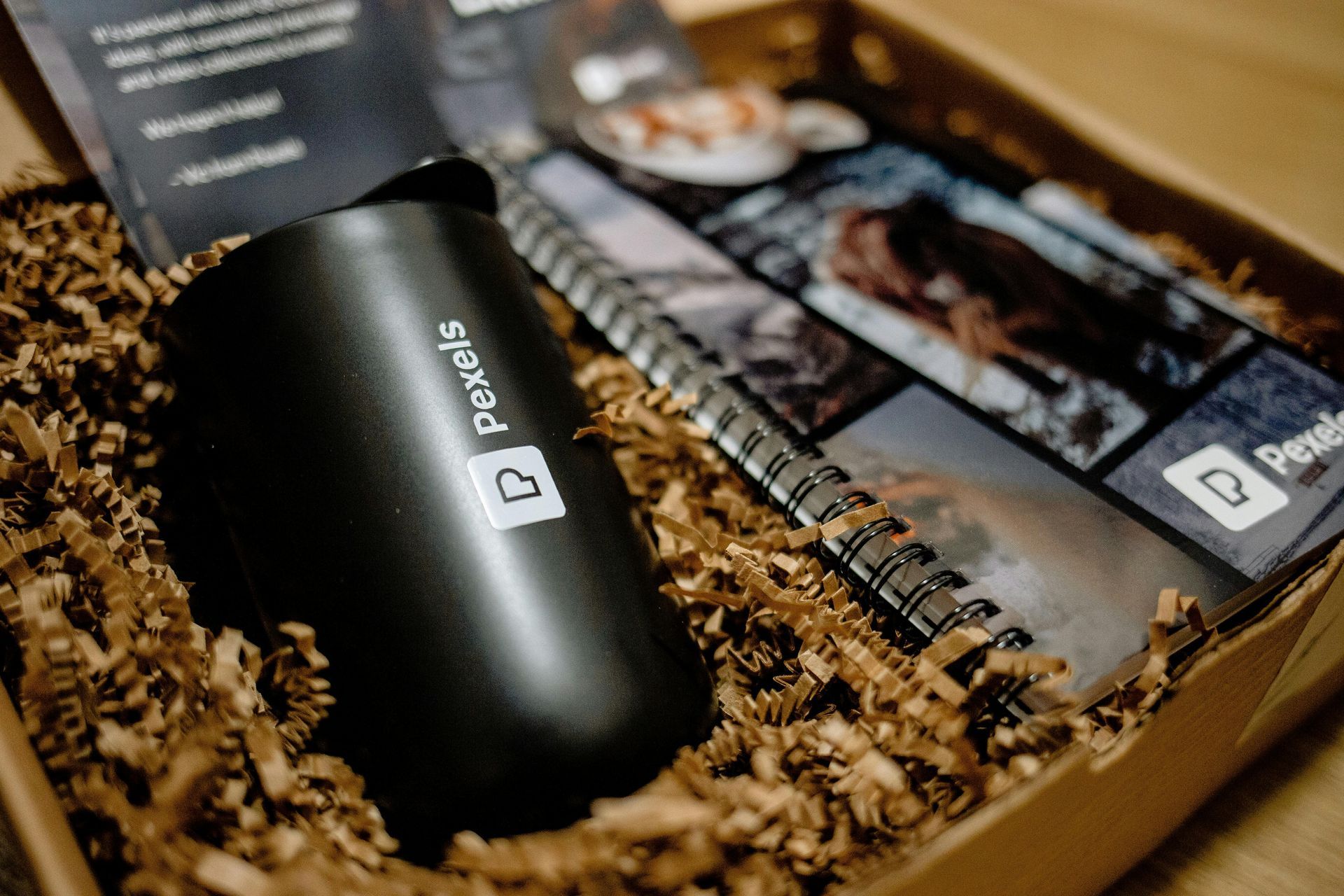 Black Pebble device in a wooden gift box with shredded paper and a brochure.