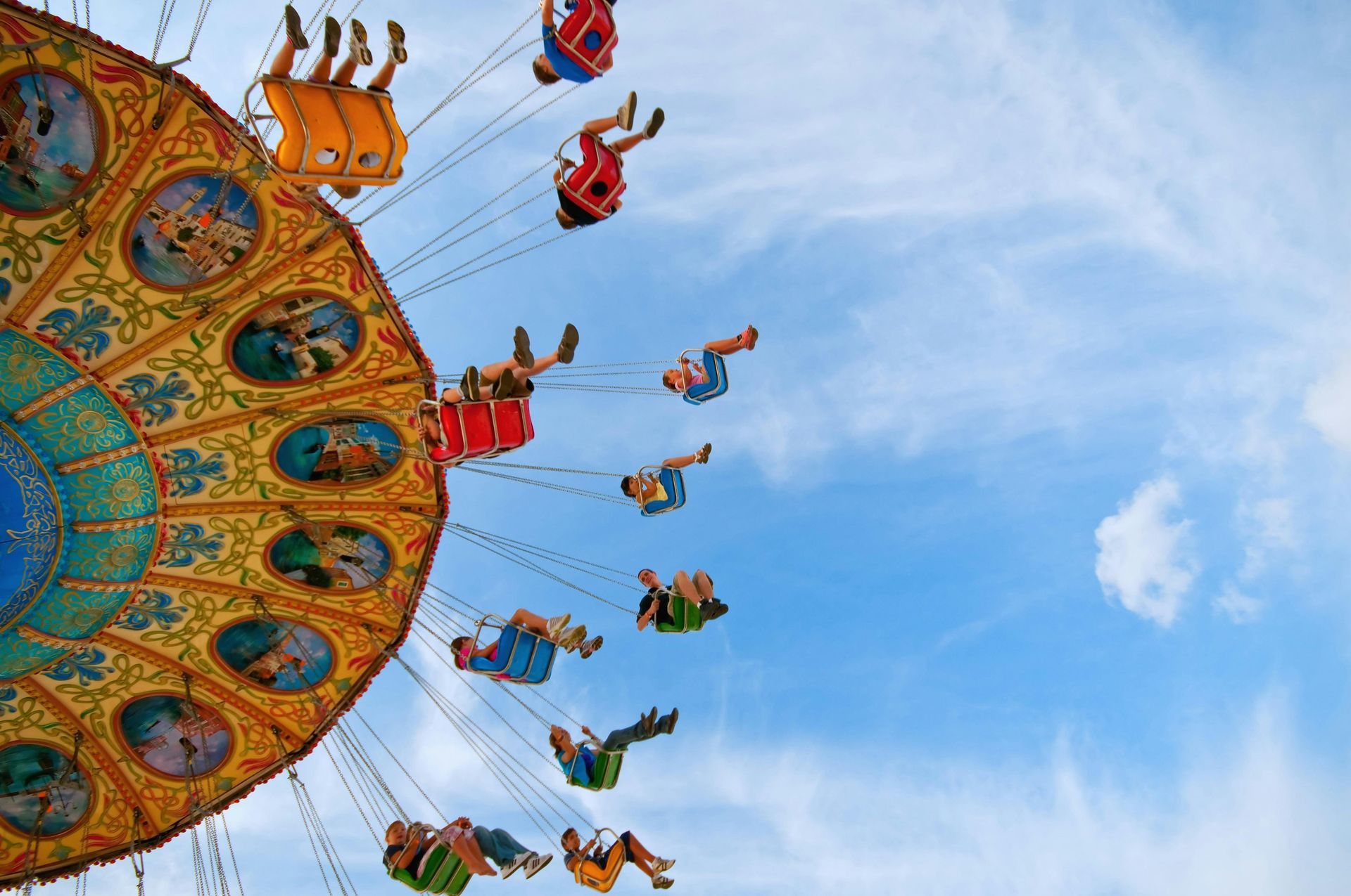 Swinging carousel ride with colorful seats against a blue sky with clouds. Passengers are suspended.